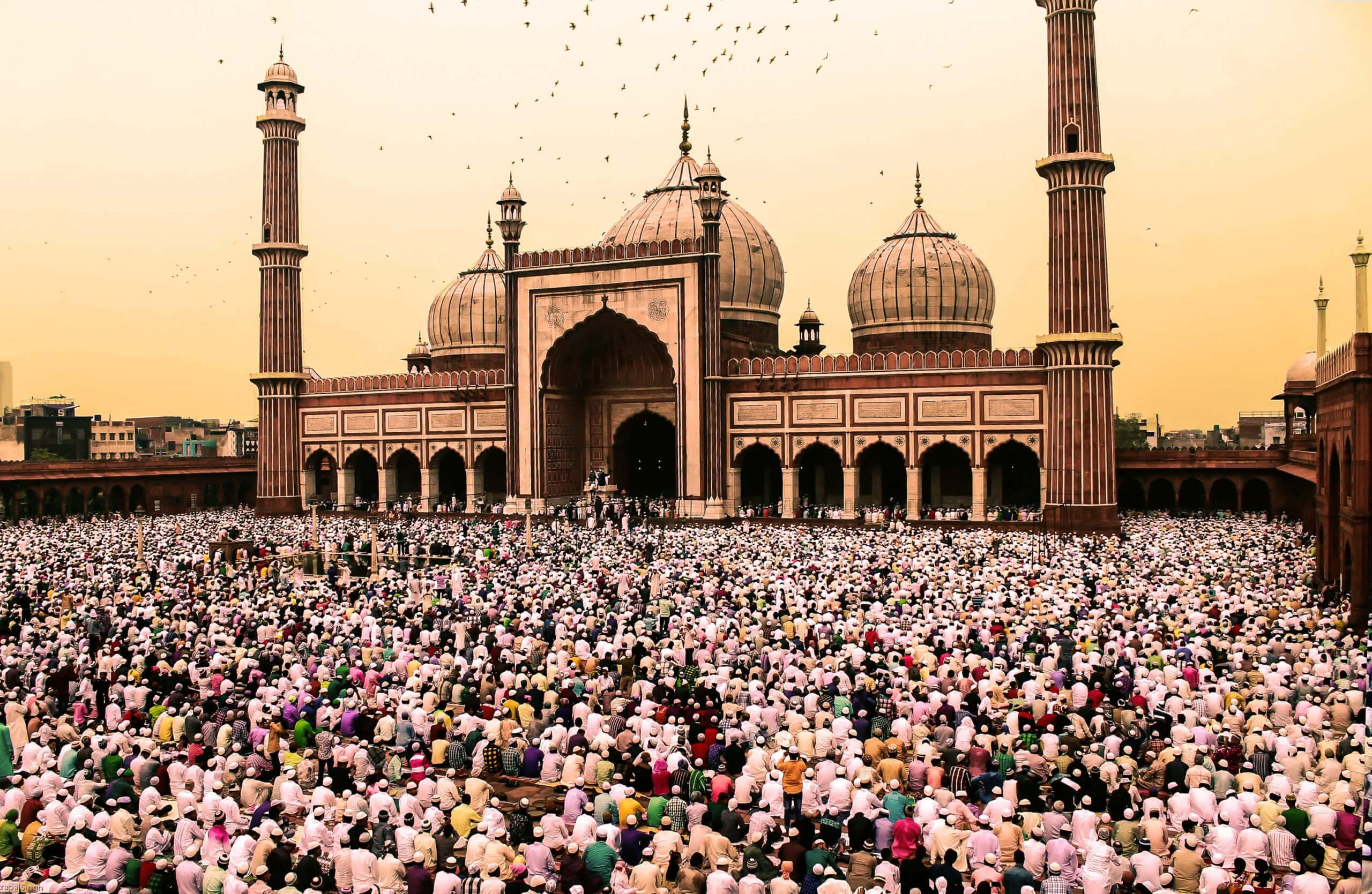 Eid 桌布 壁紙 — 大量身穿白衣的信徒在黃金時刻擠滿了擁有圓頂和宣禮塔的宏偉清真寺前的庭院。