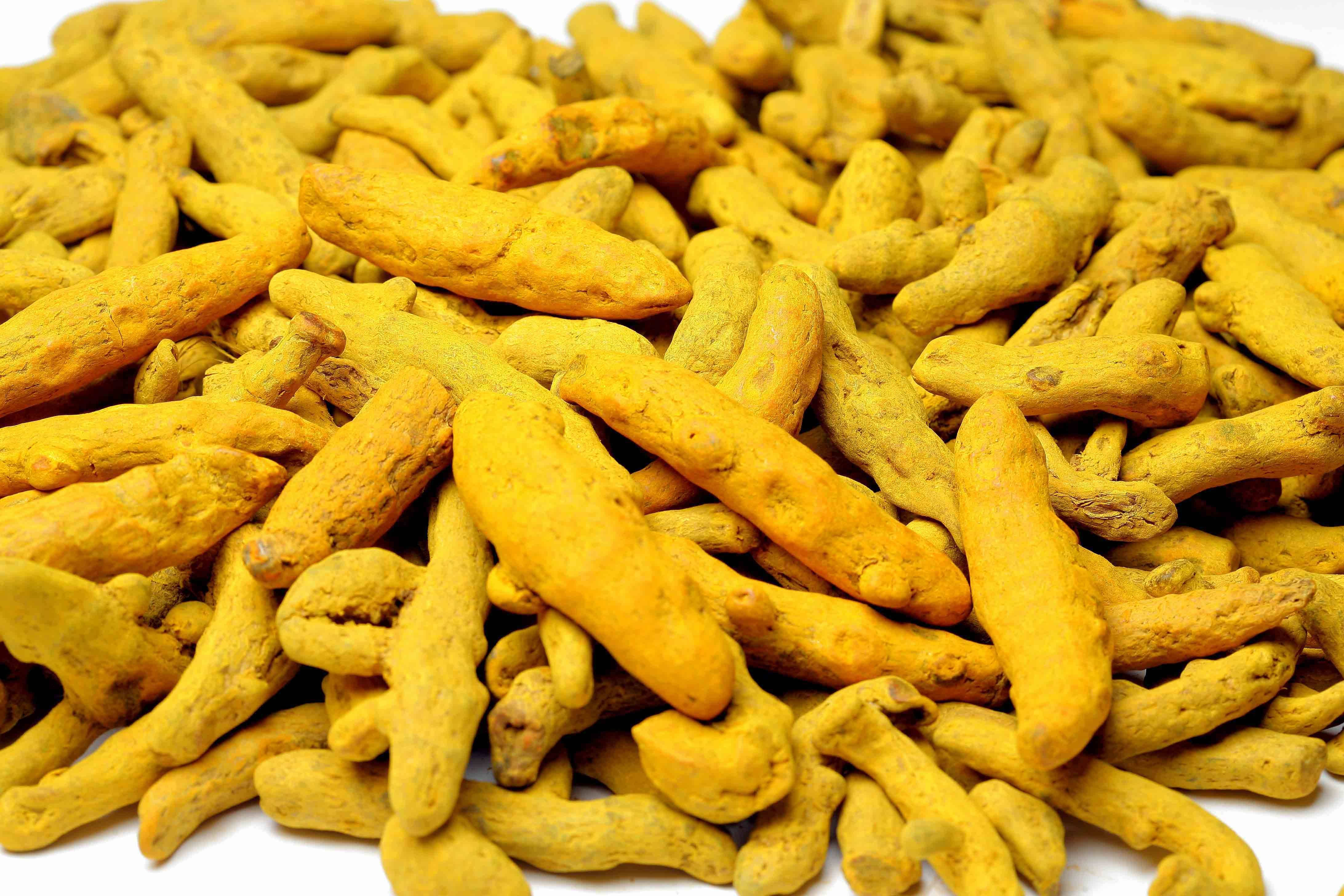 Spices 桌布 壁紙 — 大量金黃色薑黃根堆疊在純白背景上的鮮明特寫。