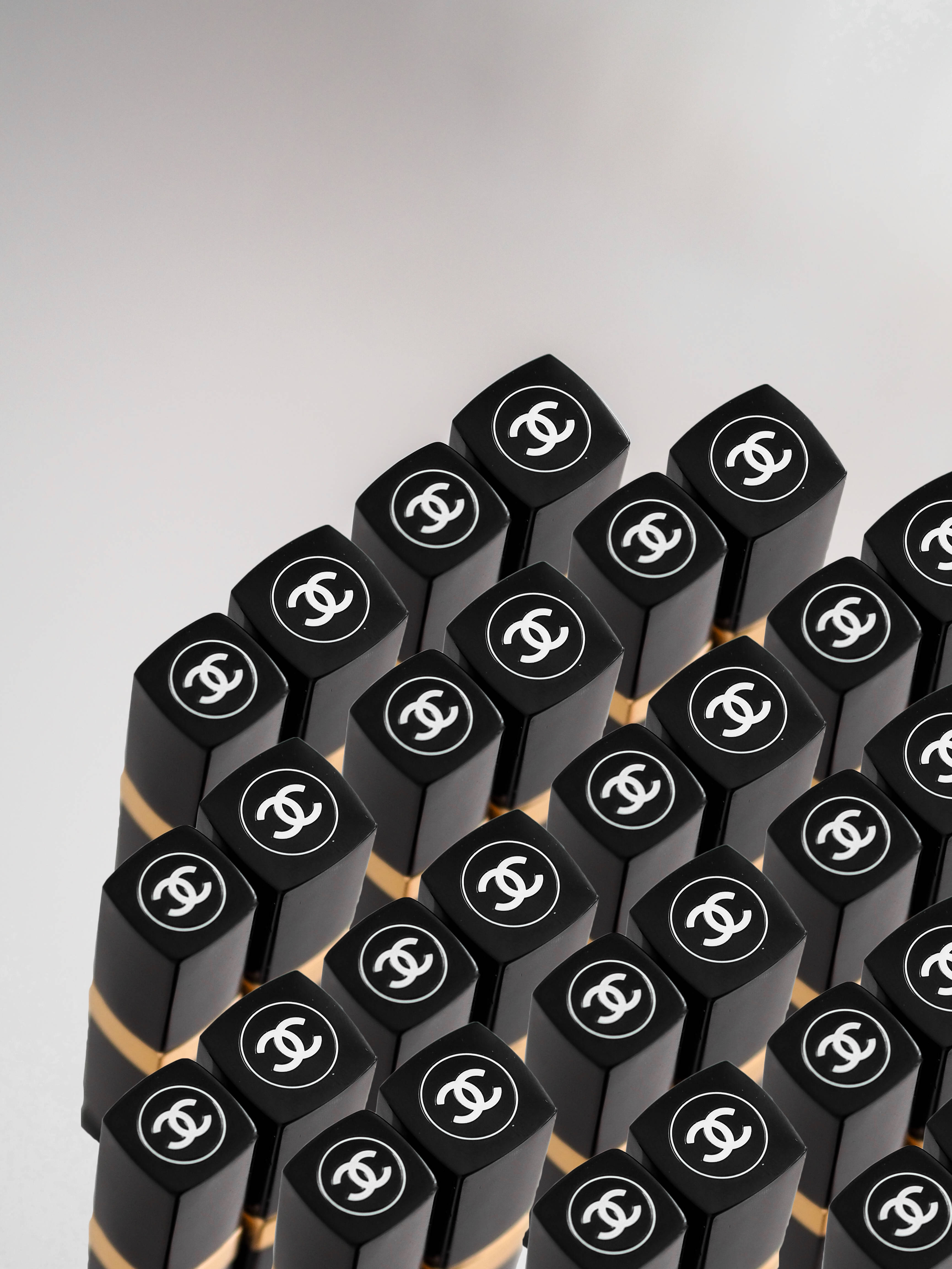 Chanel 桌布 壁紙 — 大量黑色Chanel唇膏管在柔軟灰色背景上緊密有序排列的特寫。