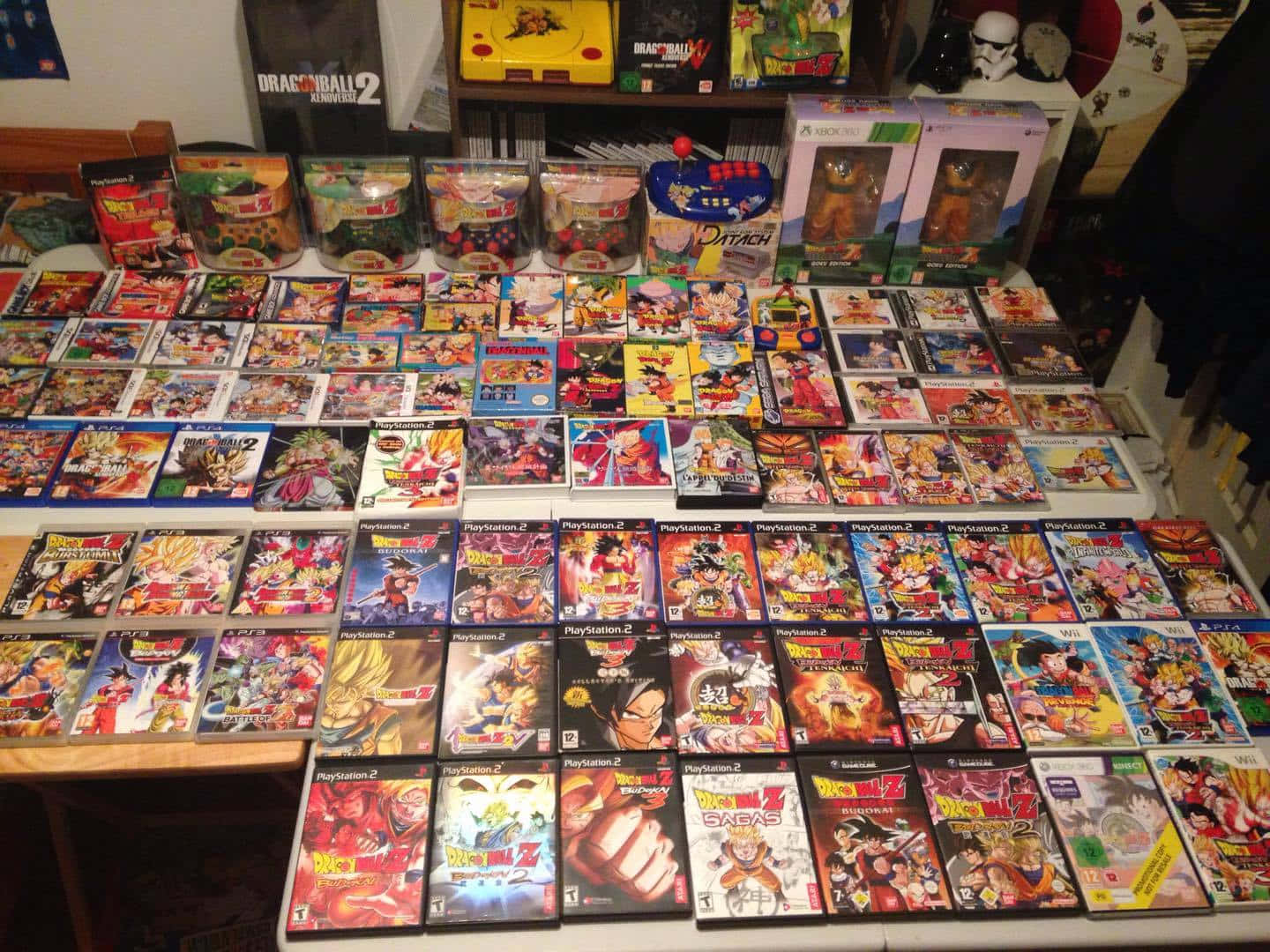 Dbz Video Games 桌布 壁紙 — 大量龍珠電玩遊戲盒整齊地排列在桌子上，周圍環繞著主題商品和主機。