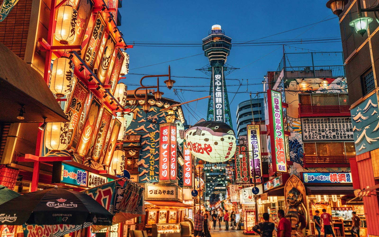 Asia 桌布 壁紙 — 大阪黃昏時分充滿活力的霓虹燈街道，高聳的燈籠和標誌性的通天塔在暮色中閃耀。