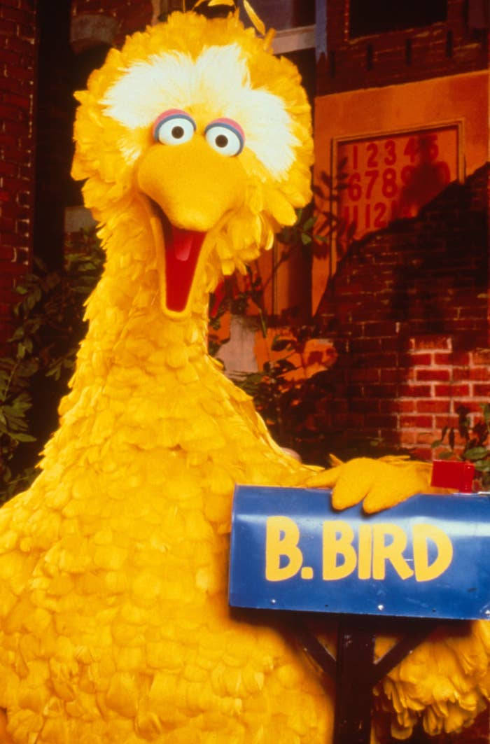 Big Bird 桌布 壁紙 — 大鳥快樂地站在磚牆前，手持一個標有B.BIRD的藍色郵箱，牆上有數字標誌。