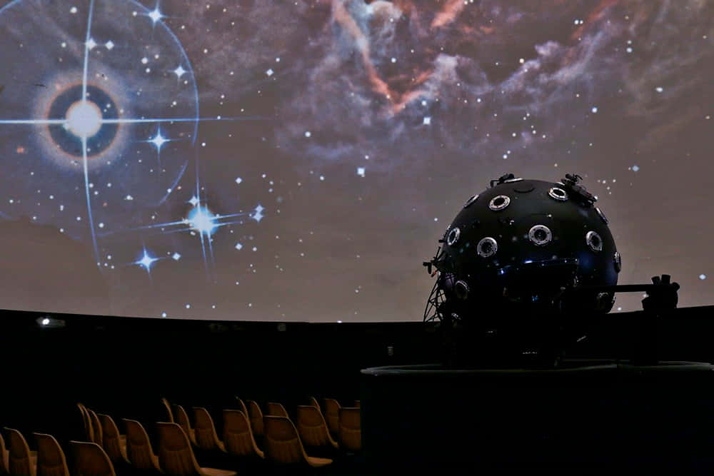 Planetarium 桌布 壁紙 — 天文館圓頂將充滿活力的星場和星雲投射到空座位上方的天花板上。
