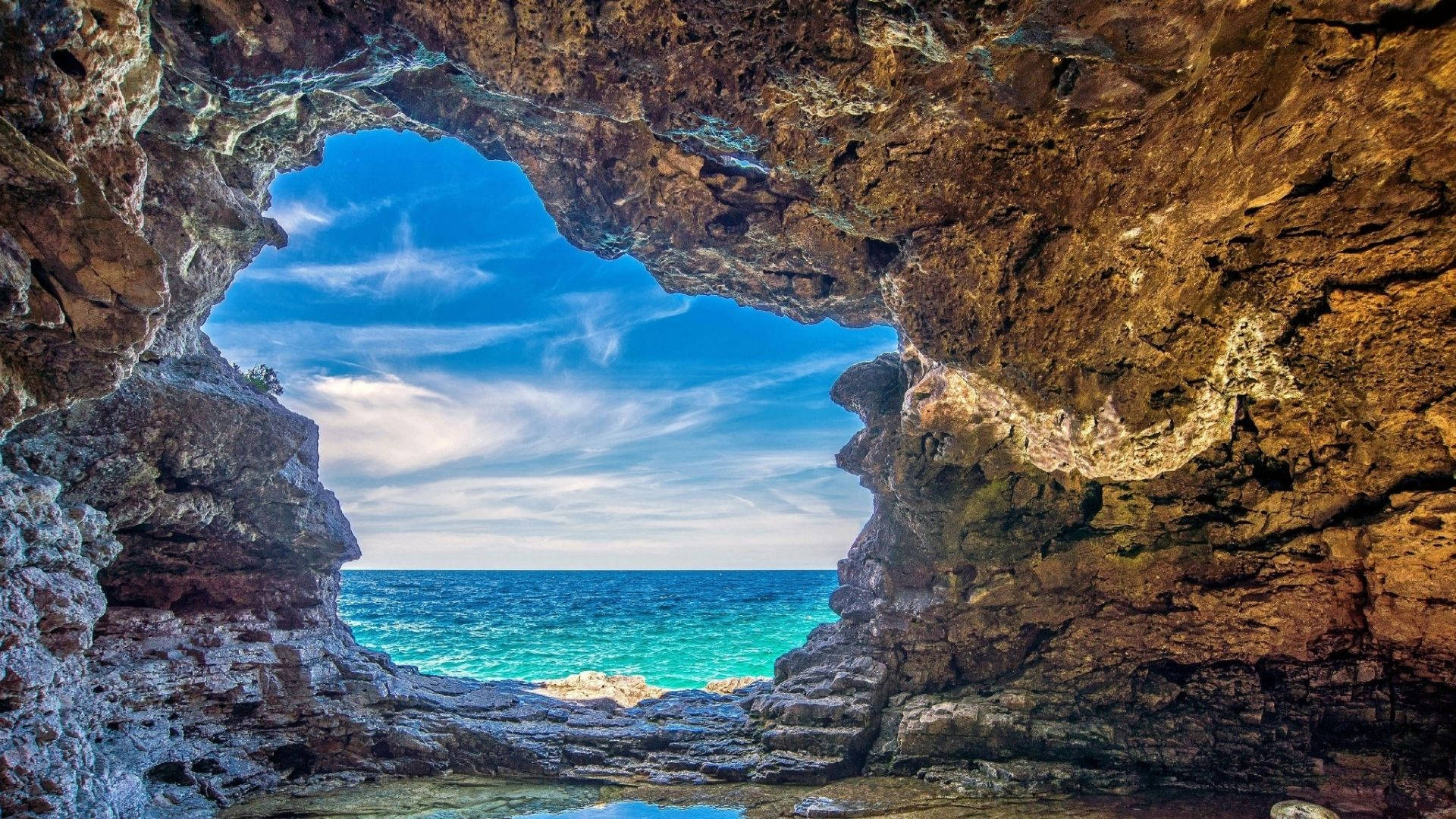 Cave 桌布 壁紙 — 天然岩石拱門框住一片充滿活力的碧綠海洋，上方是帶有縷縷白雲的明亮藍天。