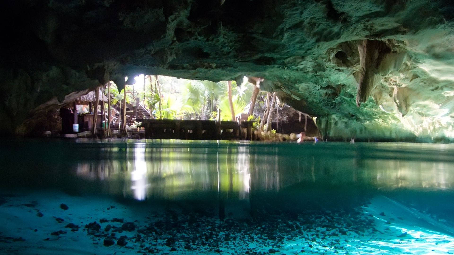 Cave 桌布 壁紙 — 天然洞穴中清澈見底的碧綠海水，陽光穿過洞口照射進來，露出外面茂密的綠色叢林。
