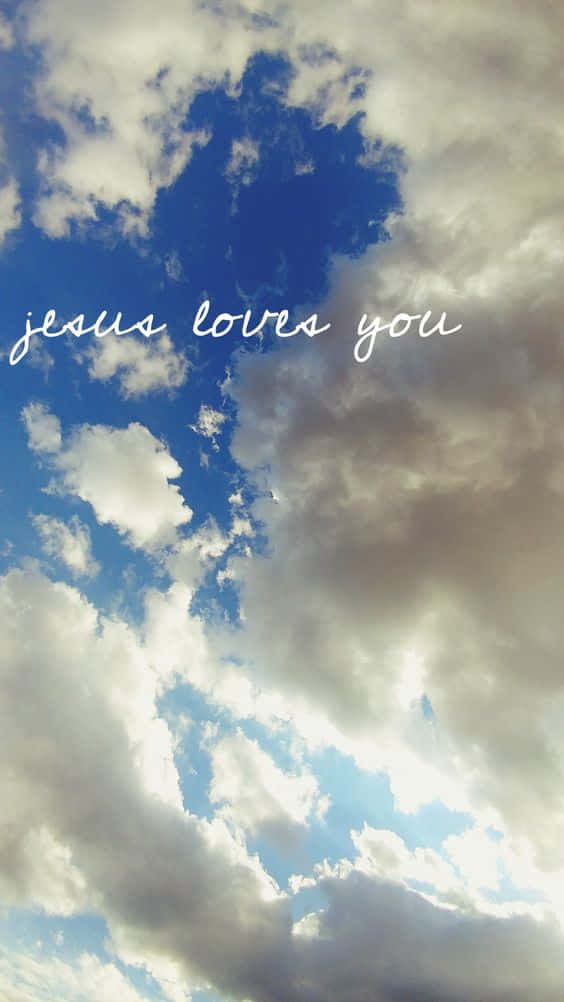 God Loves You 桌布 壁紙 — 天空中有蓬鬆的白雲和深藍色斑塊，上面有白色草書文字 'jesus loves you'。