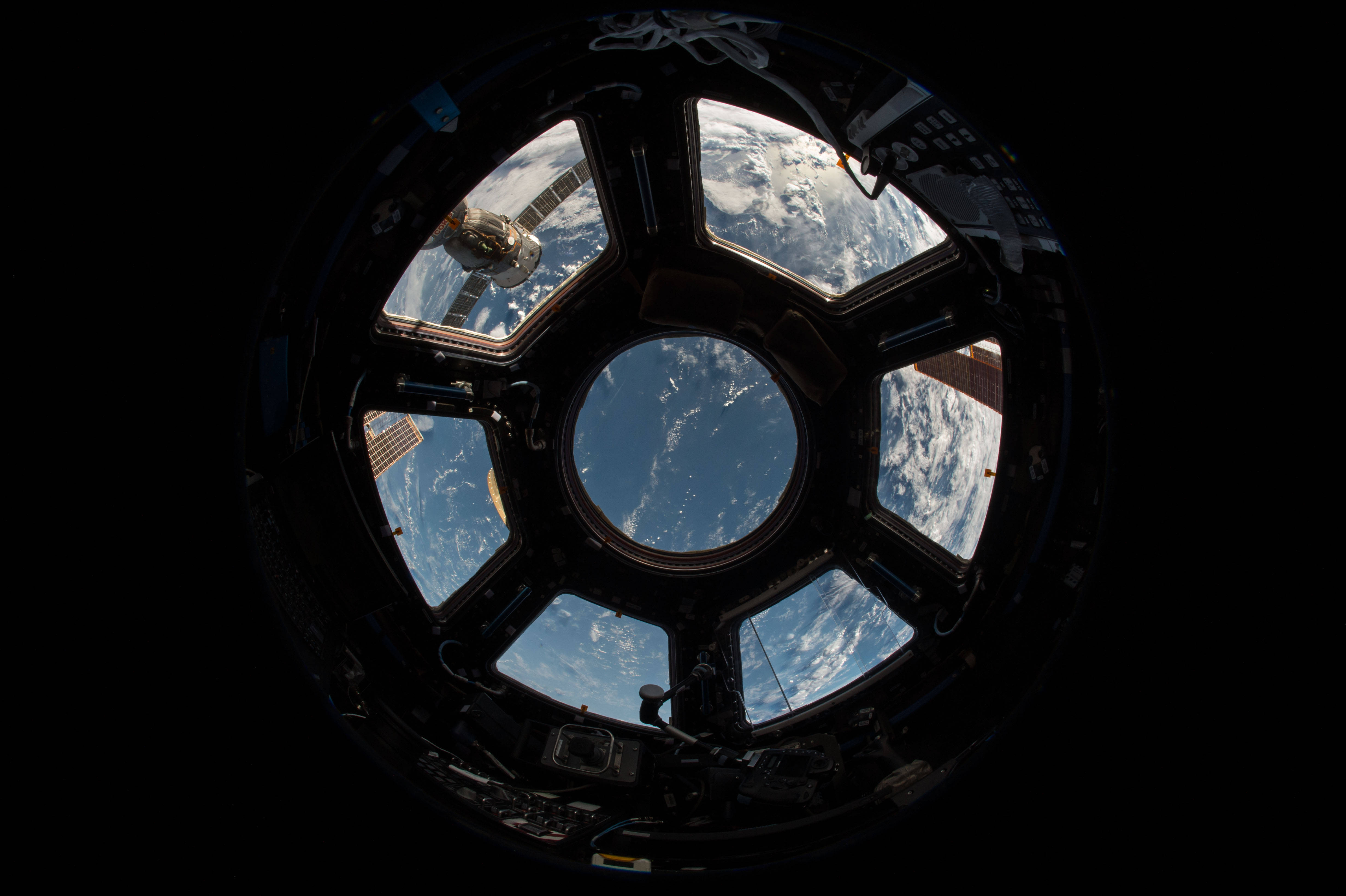 太空 桌布 壁紙 — 太空船內的圓形窗戶揭示了地球的藍色海洋和白色雲朵，背景是太空的黑色虛空。