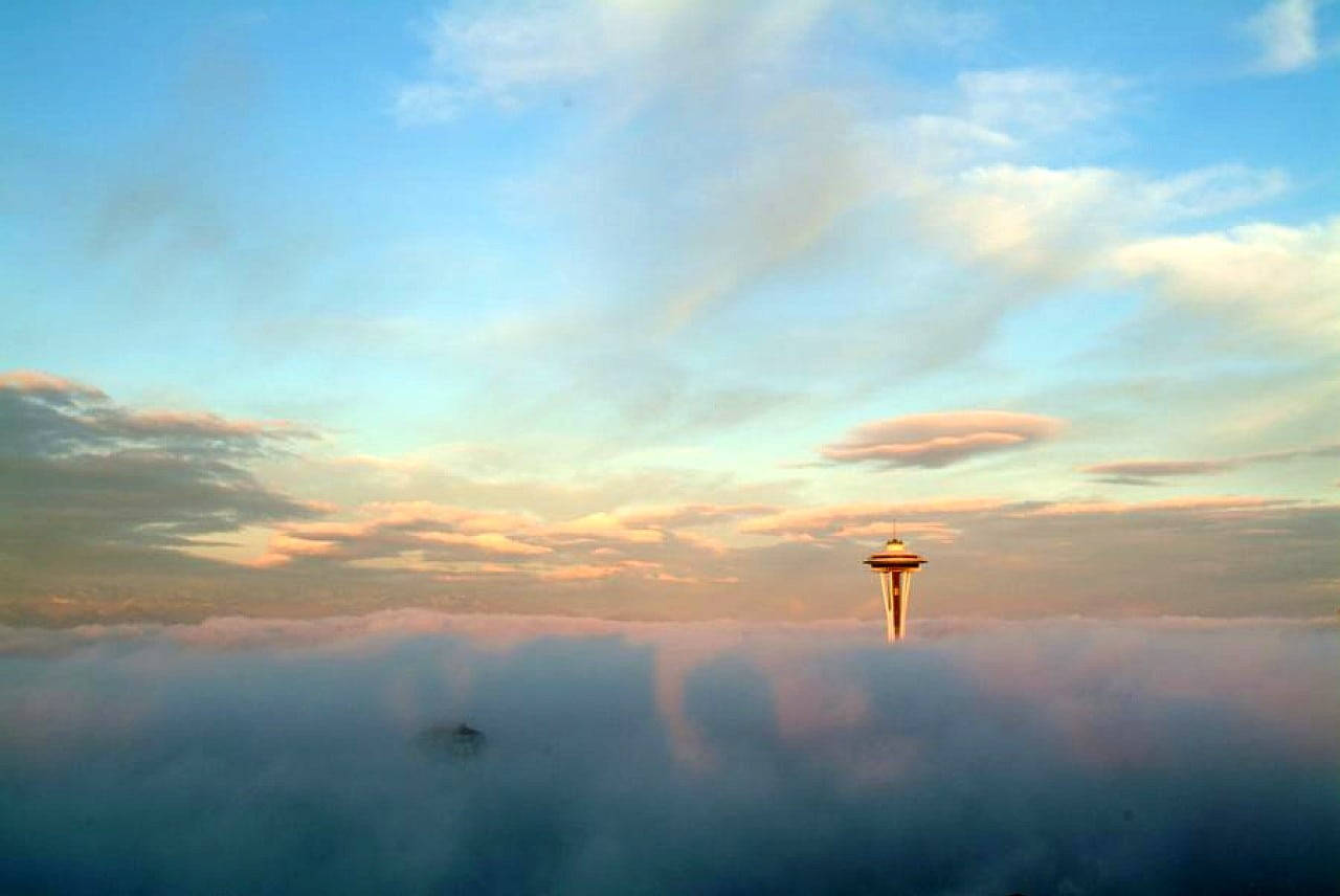 Space Needle 桌布 壁紙 — 太空針塔在日出時刺穿雲海，柔和的粉紅色和藍色色調描繪天空。