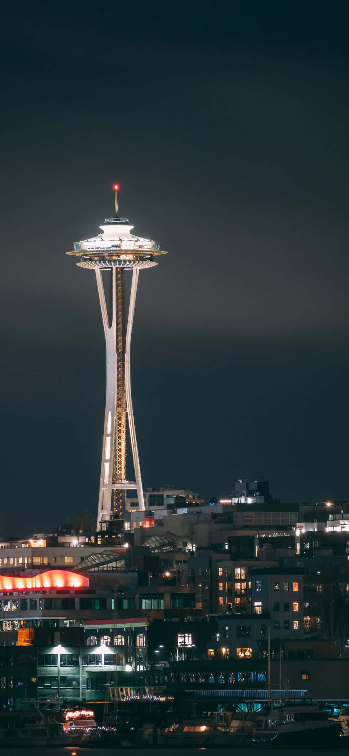 iPhone X Seattle 桌布 壁紙 — 太空針塔在黑暗的夜空中閃耀，下方是西雅圖燈火通明的海濱建築。
