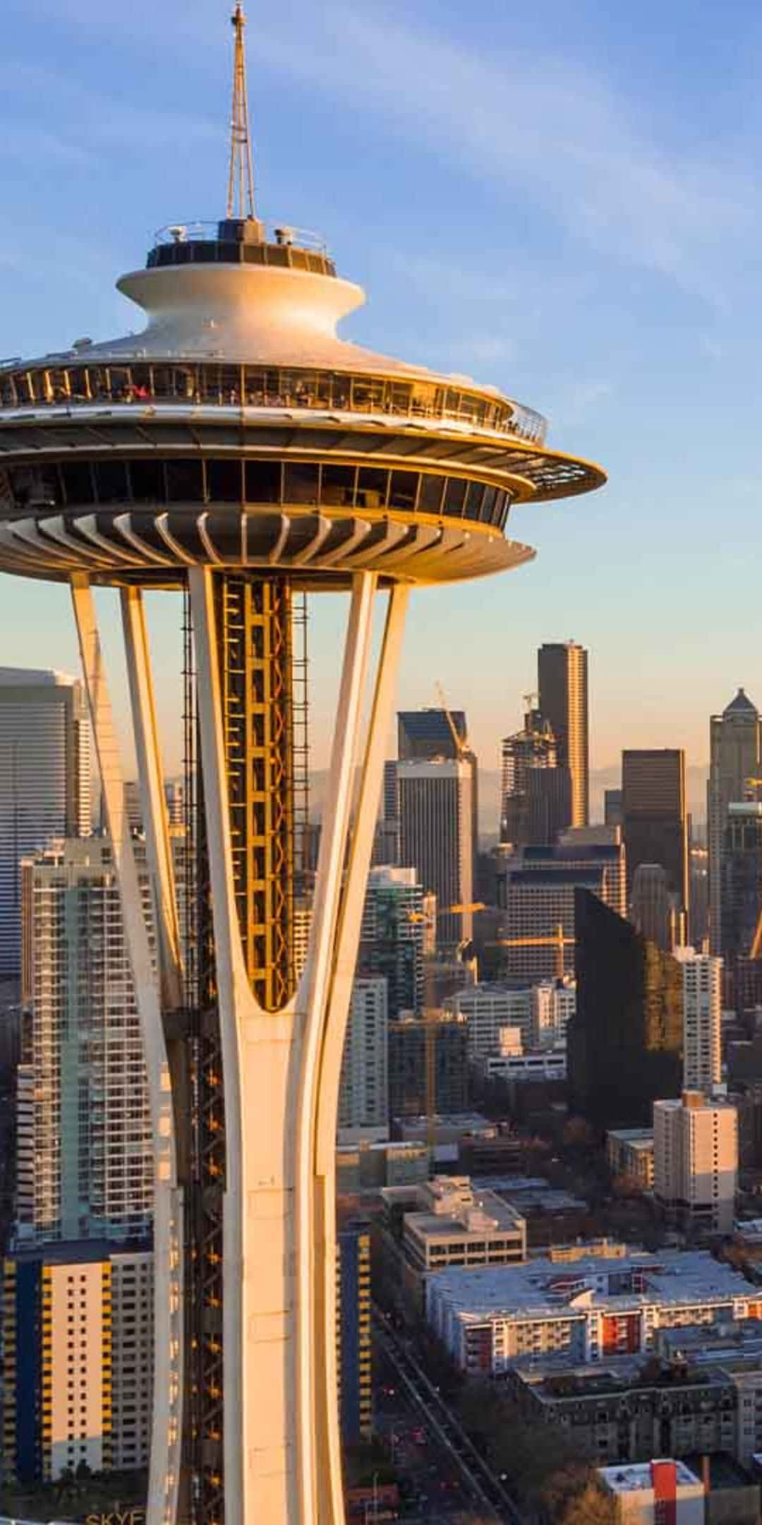 Pixel 3 Seattle 桌布 壁紙 — 太空針塔沐浴在金色日落光芒中，聳立於西雅圖的城市天際線之上，摩天大樓延伸至清澈的藍天。