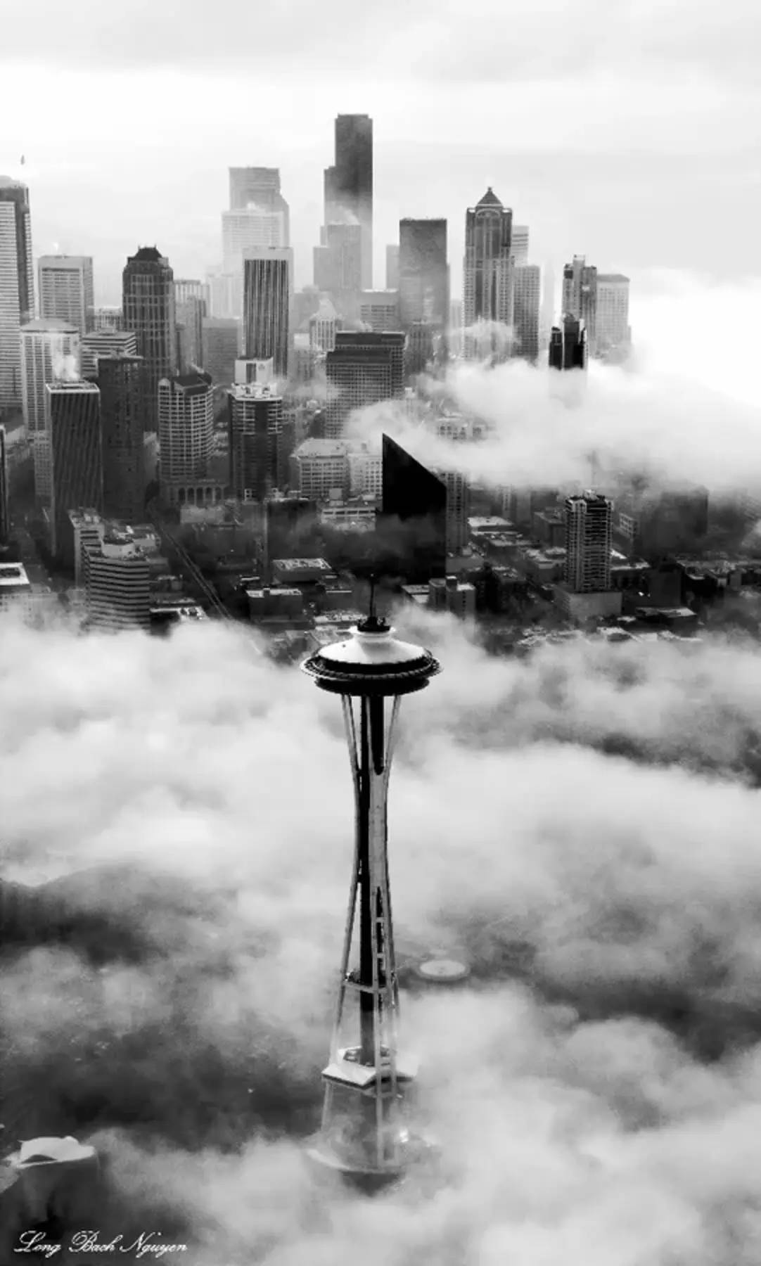西雅圖 iPhone 桌布 壁紙 — 太空針塔穿過濃密雲層的單色航拍圖，背景是霧氣瀰漫的西雅圖天際線。