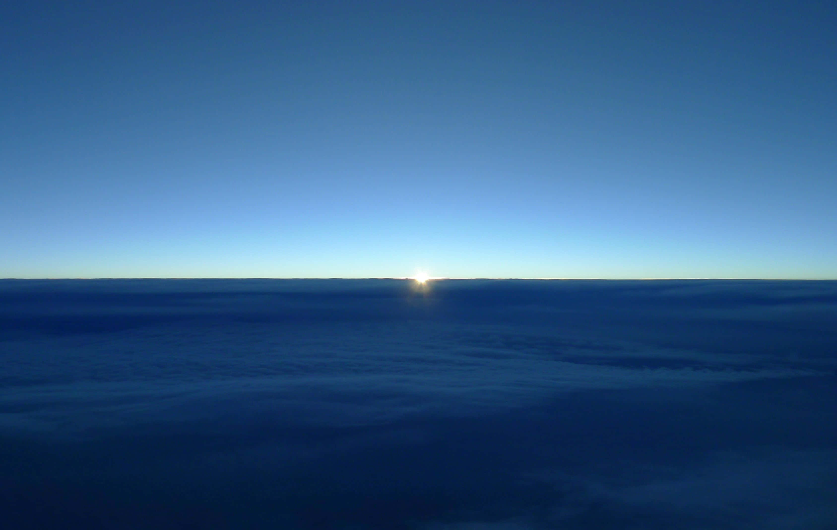 Minimalist Ocean 桌布 壁紙 — 太陽在無邊無際的雲海上升起，在地平線上投下柔和的藍色光芒。