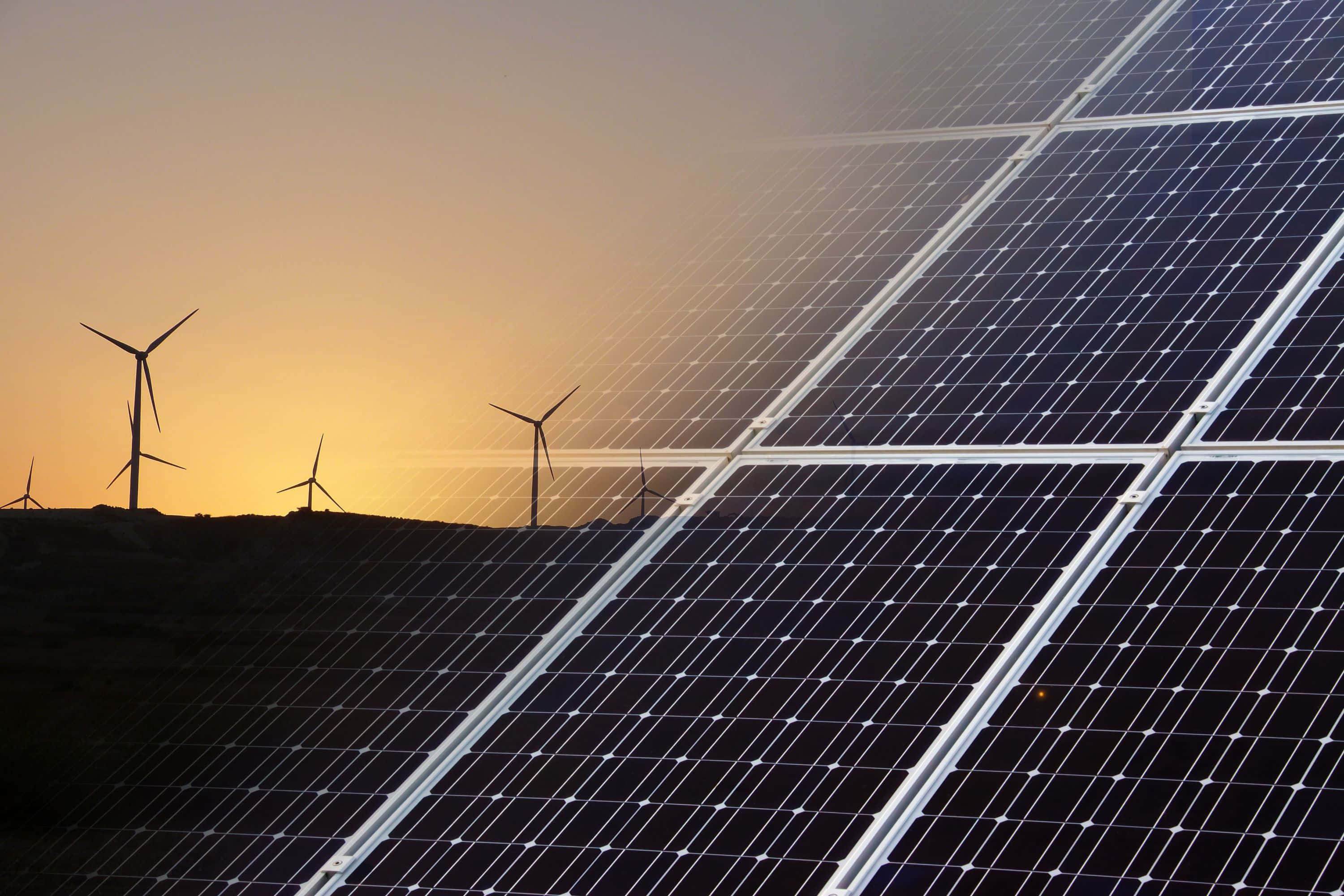 Renewable Energy 桌布 壁紙 — 太陽能板主導前景，風力渦輪機在溫暖的日落天空襯托下形成剪影。