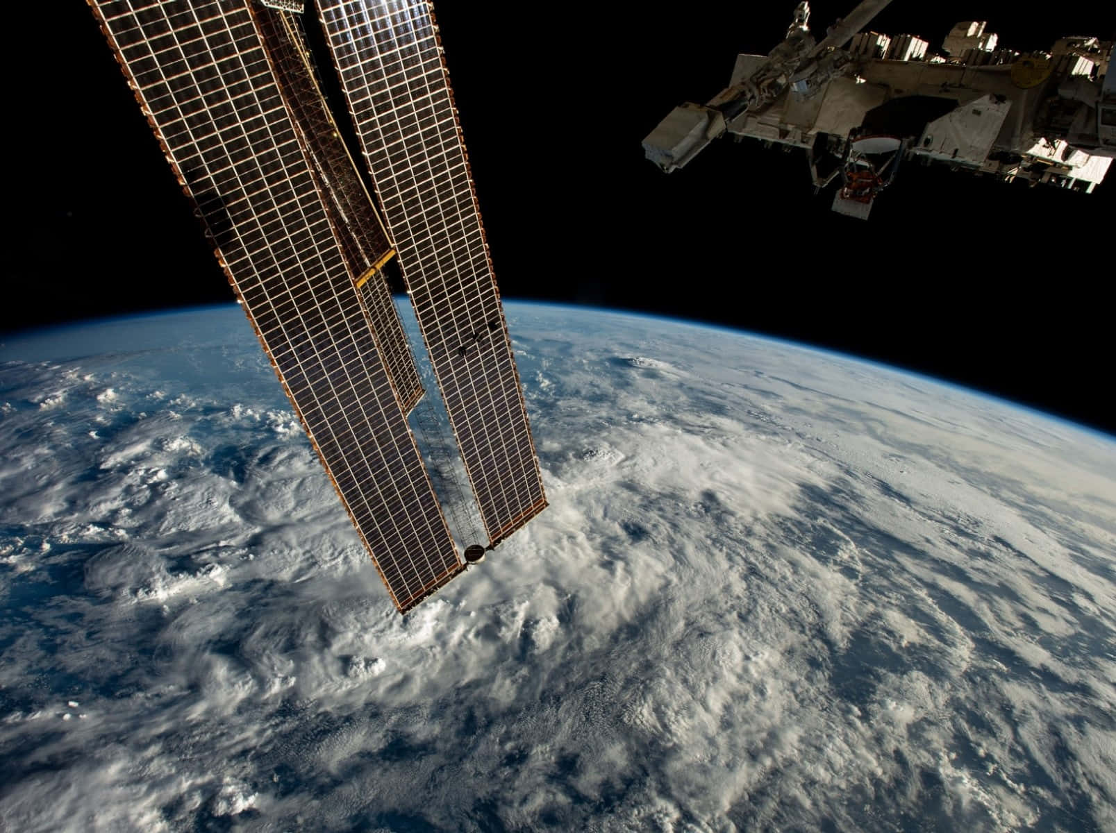 Space Satellite 桌布 壁紙 — 太陽能電池板和太空站模組在旋轉的藍白地球上方，向著黑色虛空延伸。
