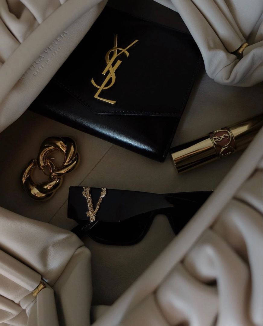 Designer Logo 桌布 壁紙 — 奢華YSL配件置於奶油色米色布料中，搭配金色點綴和黑色皮革。