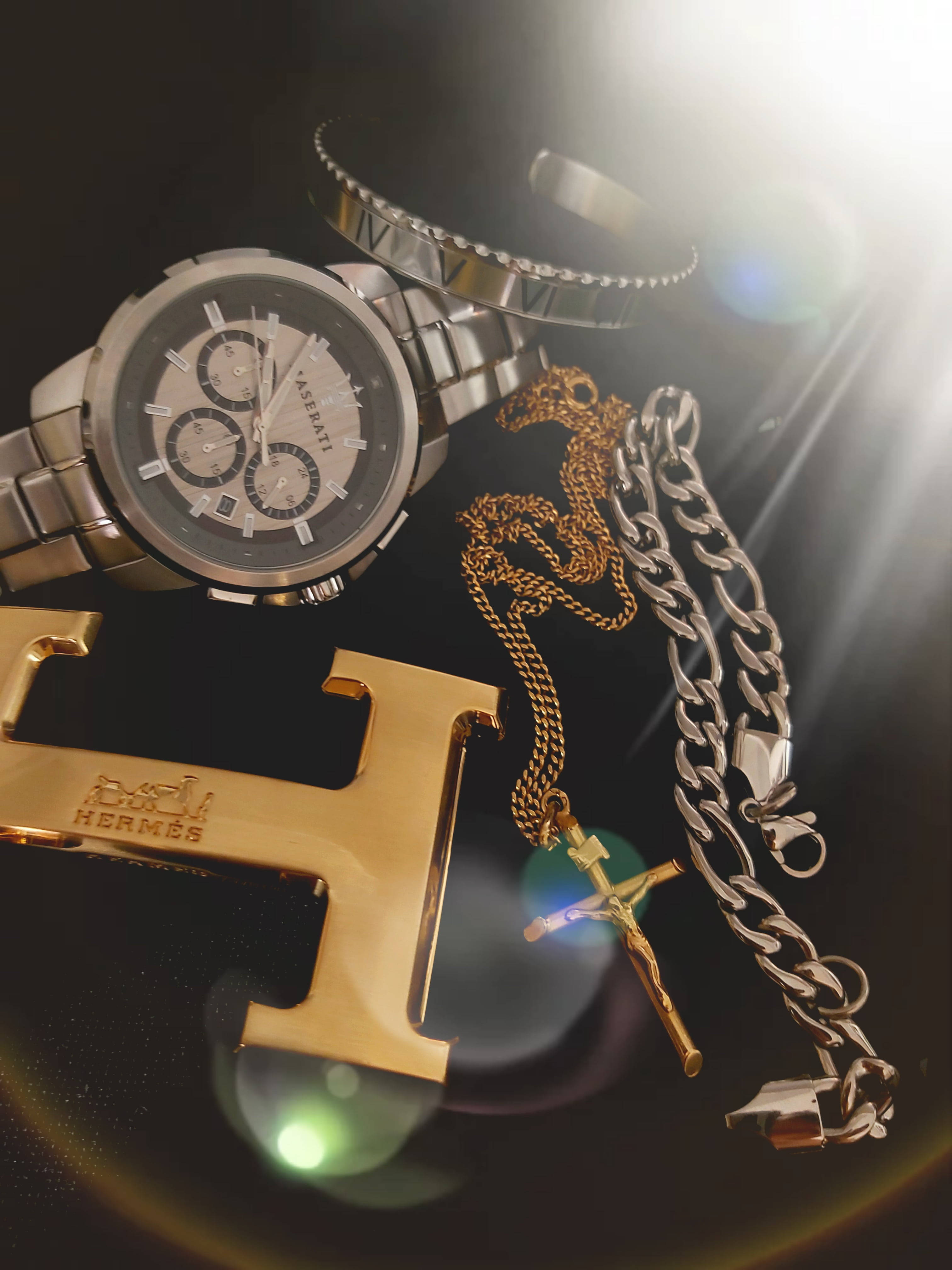 Hermes 桌布 壁紙 — 奢華配件，包括銀色手錶、金鏈和愛馬仕皮帶扣，在戲劇性的背光下閃閃發光。