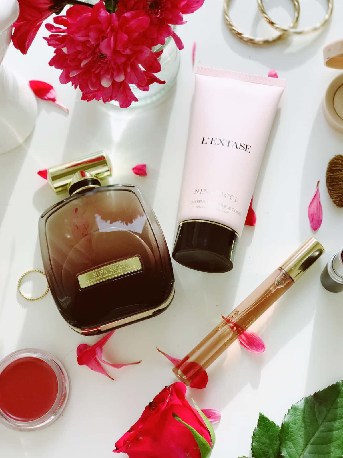 Spring Perfume 桌布 壁紙 — 奢華香水及護膚產品，搭配鮮豔粉紅花朵與金色首飾，在明亮的白色表面上藝術地擺放。