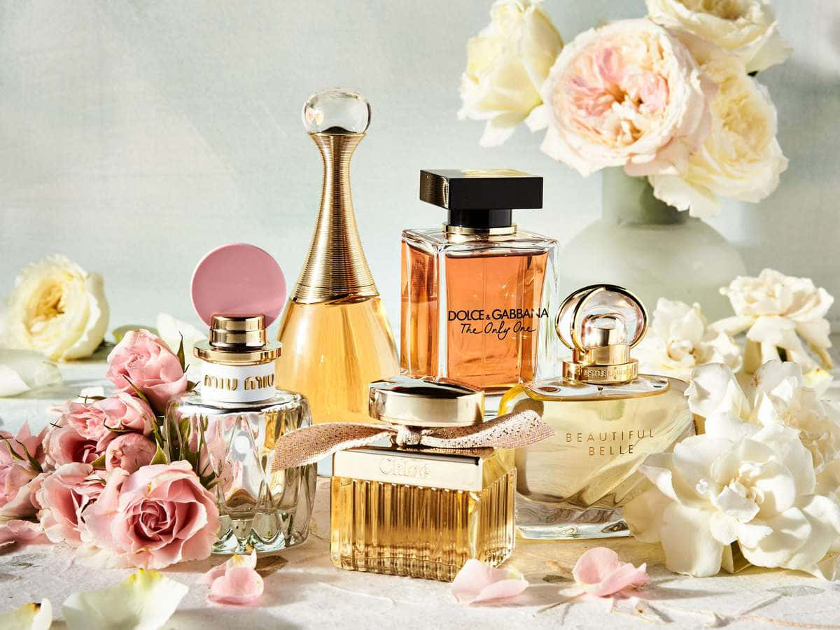 Spring Perfume 桌布 壁紙 — 奢華香水瓶優雅地排列在柔和的粉紅和白色玫瑰之間，置於有紋理的表面上。