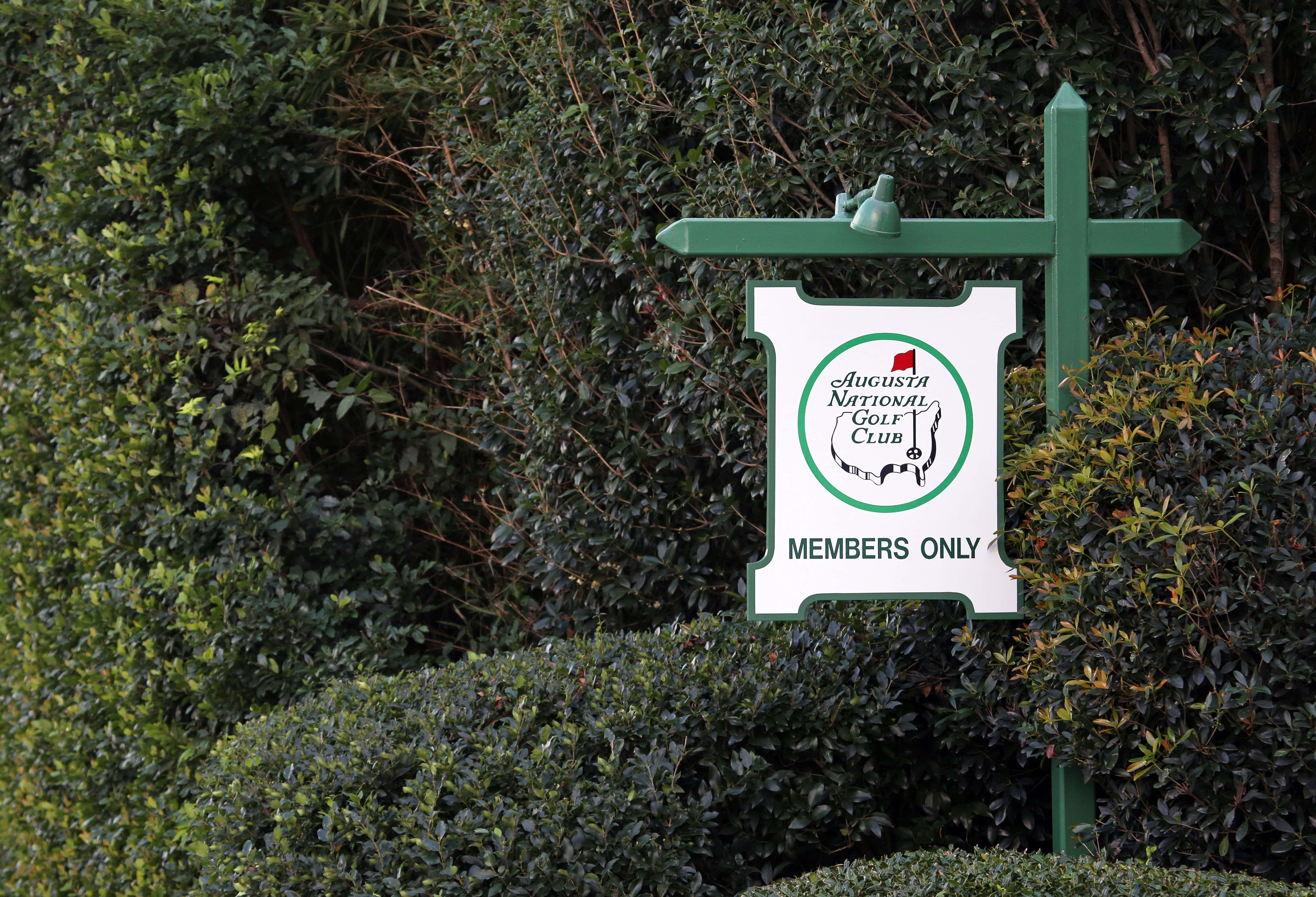 Augusta National iPhone 桌布 壁紙 — 奧古斯塔國家高爾夫俱樂部的一個綠色框標誌，上面寫著「僅限會員」，矗立在茂密的深綠色樹籬中。
