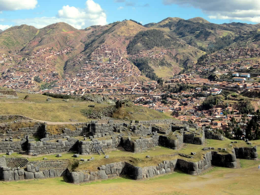 Historical 桌布 壁紙 — 奧揚泰坦博的古代石遺跡位於前景，梯田山城和綠色山丘在藍天下。