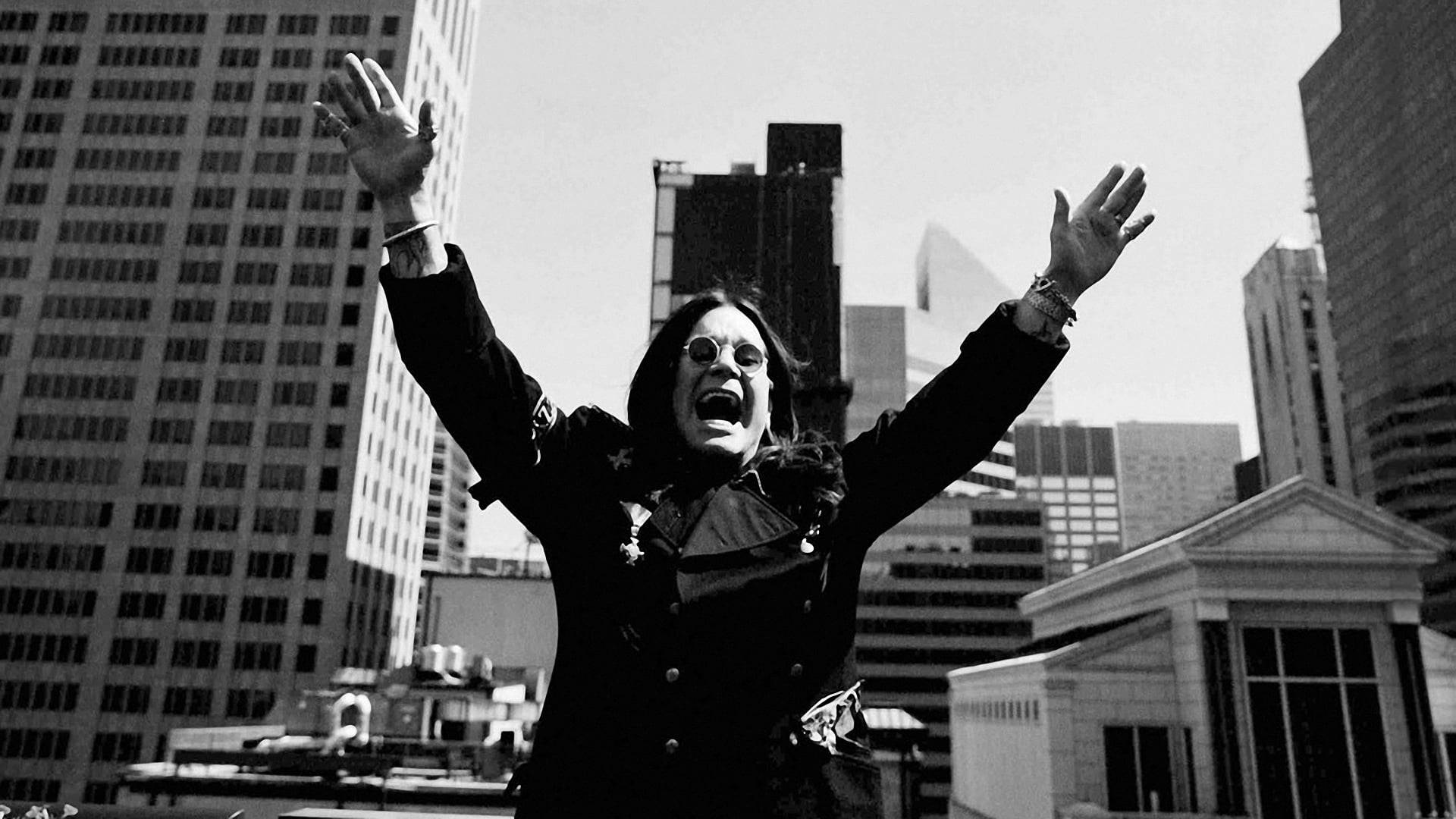 Ozzy Osbourne 桌布 壁紙 — 奧茲·奧斯本站在屋頂上，高舉雙臂，背景是聳立的城市摩天大樓，一張戲劇性的黑白照片。
