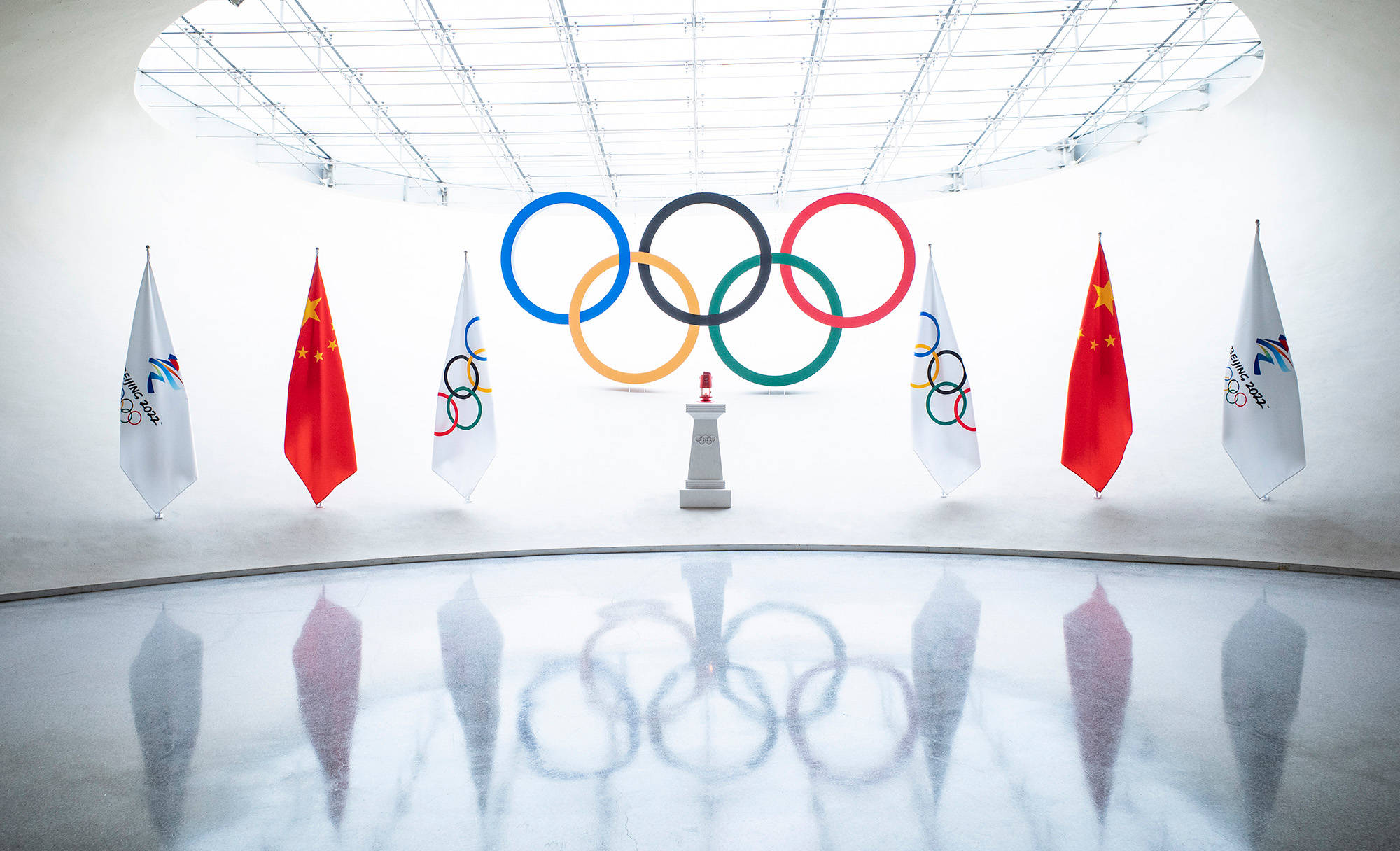 Winter Olympics 桌布 壁紙 — 奧運五環懸掛在明亮的白色圓頂內，中國國旗和奧運旗幟反射在拋光地板上。