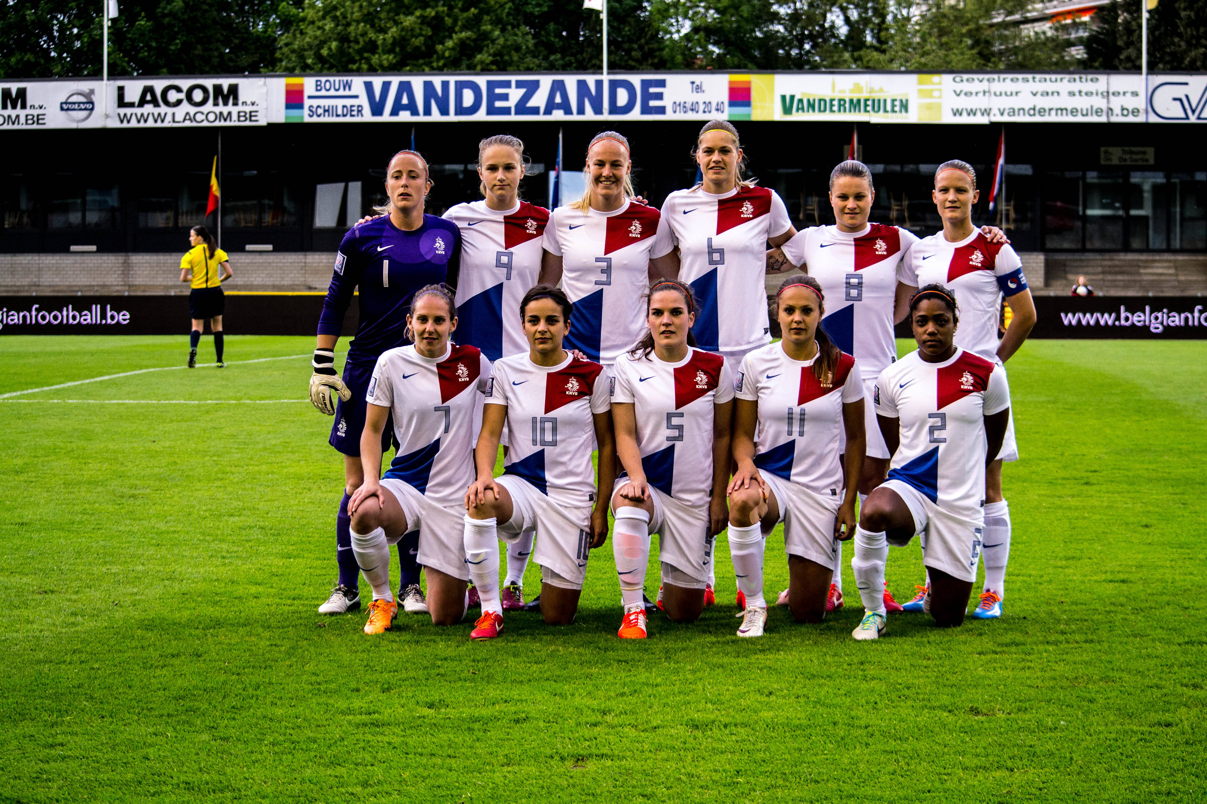 Netherlands 桌布 壁紙 — 女子足球隊穿著白色、紅色和藍色球衣，在明亮的日光下於充滿活力的綠色球場上擺姿勢。