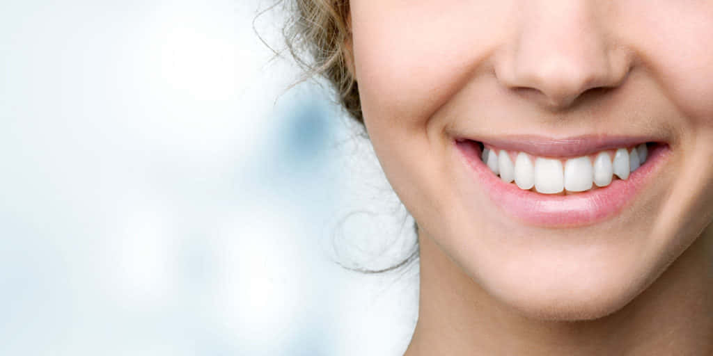 Smile 桌布 壁紙 — 女性燦爛笑容的特寫，展現完美潔白的牙齒，背景是柔和模糊的藍色。