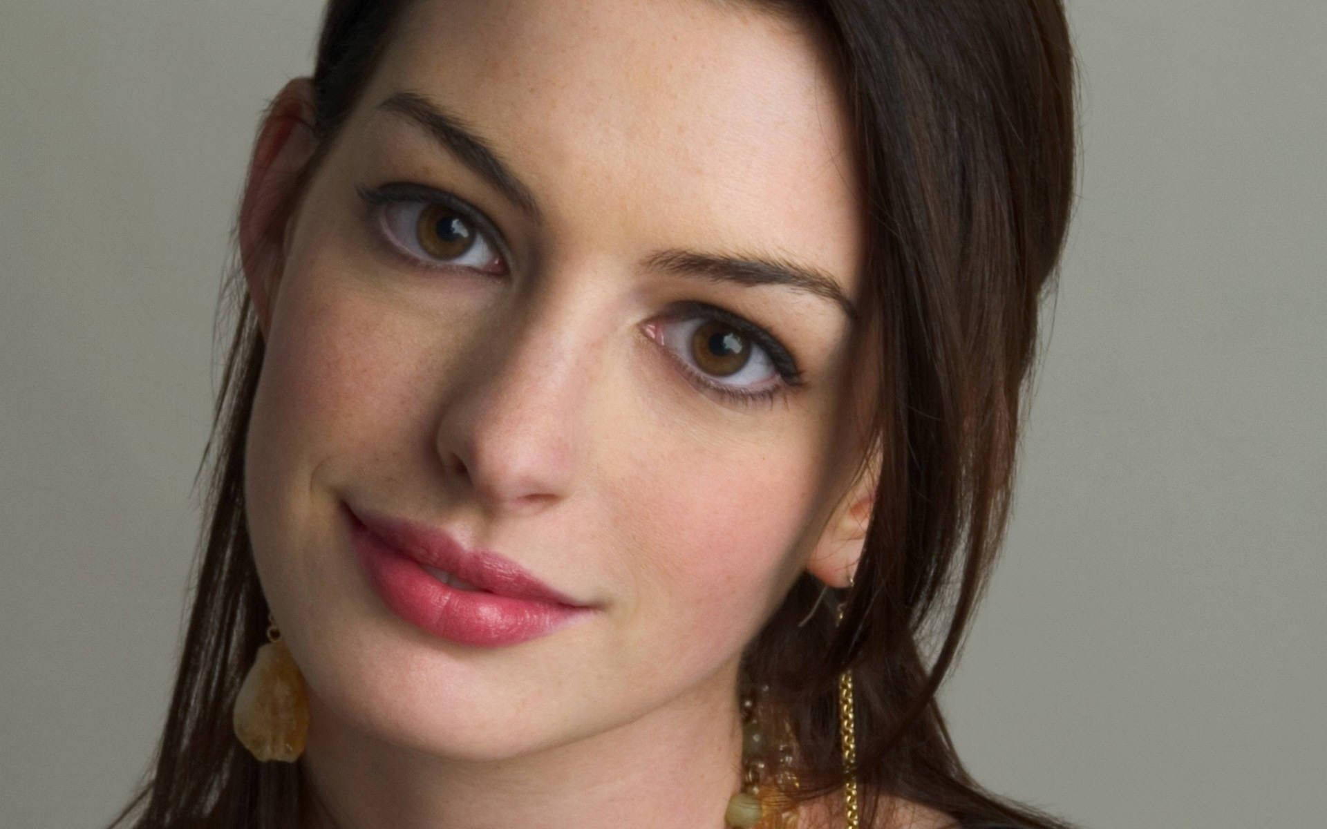 Anne Hathaway 桌布 壁紙 — 女性特寫肖像，擁有溫暖的棕色眼睛和柔和微笑，背景為中性灰色。
