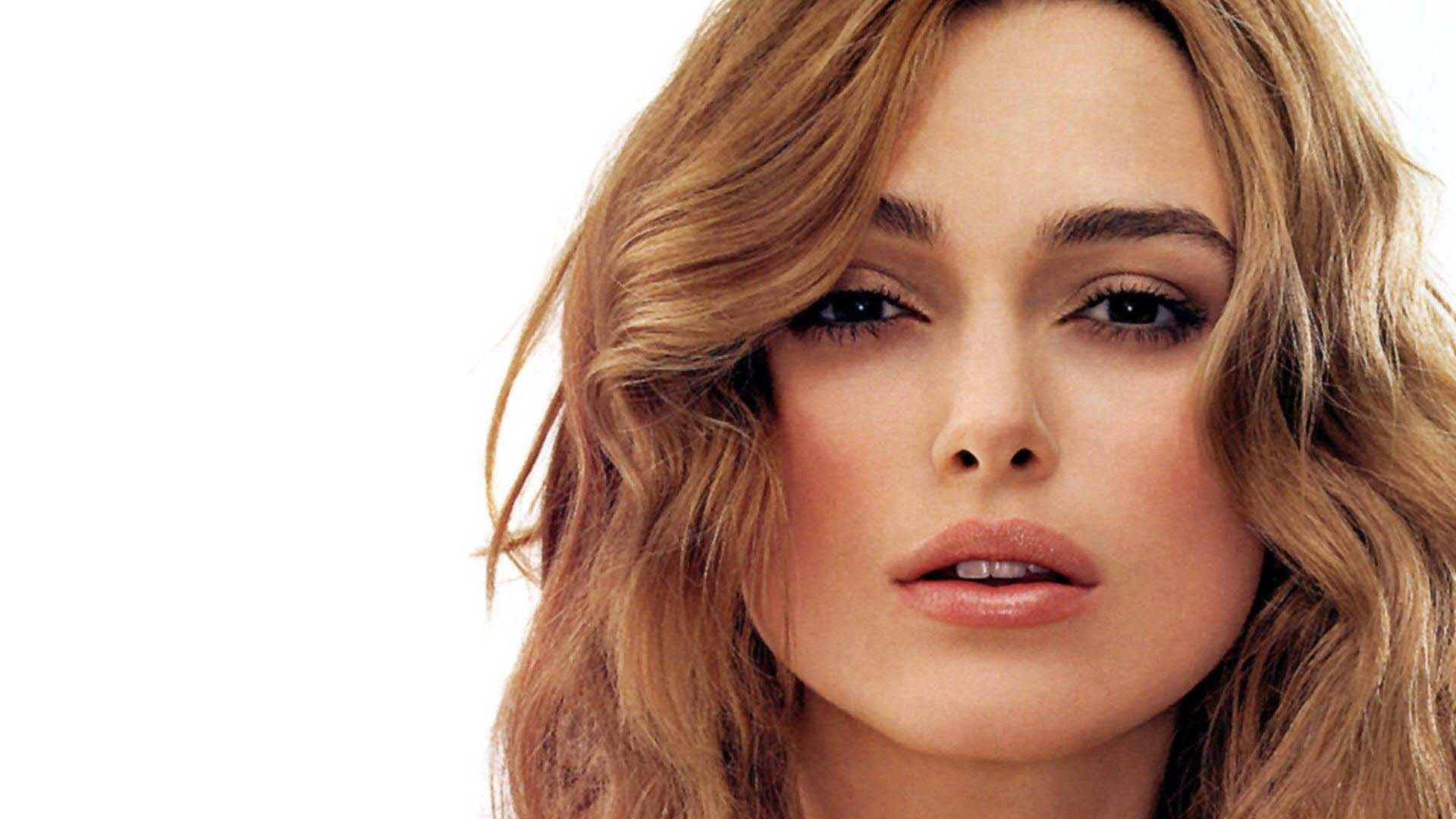 Keira Knightley 桌布 壁紙 — 女性特寫肖像，波浪形金髮和柔和化妝，背景為純白色。