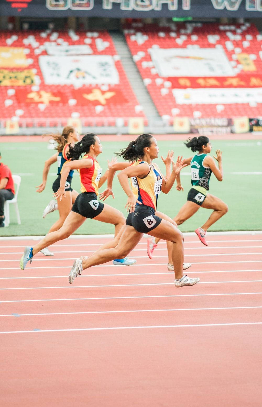 Athletic 桌布 壁紙 — 女性短跑選手在紅色跑道上激烈比賽，背景有模糊的動作和體育場座位。