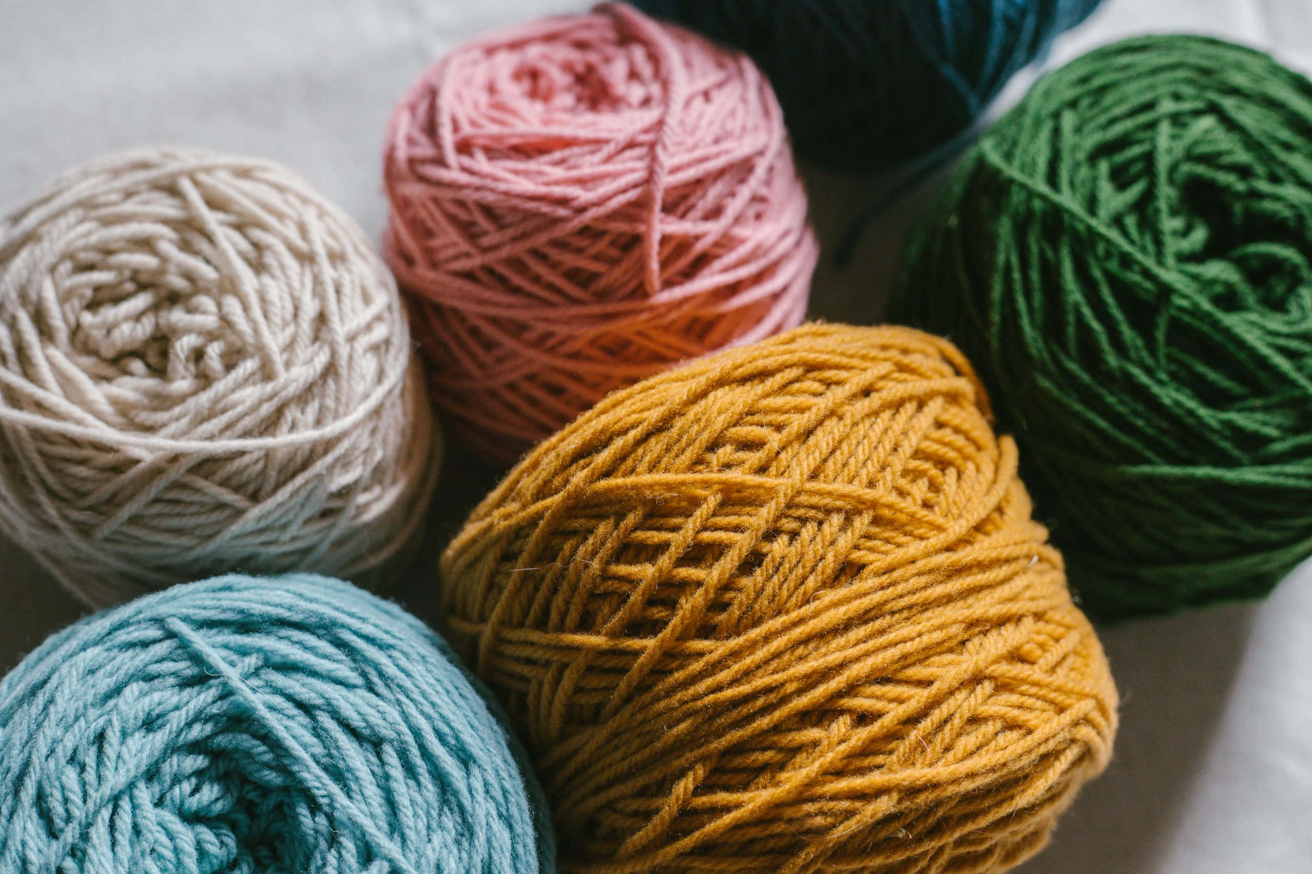 Knitting 桌布 壁紙 — 奶油色、粉紅色、芥末色、綠色和藍綠色的彩色毛線球特寫，排列在柔軟的白色表面上。