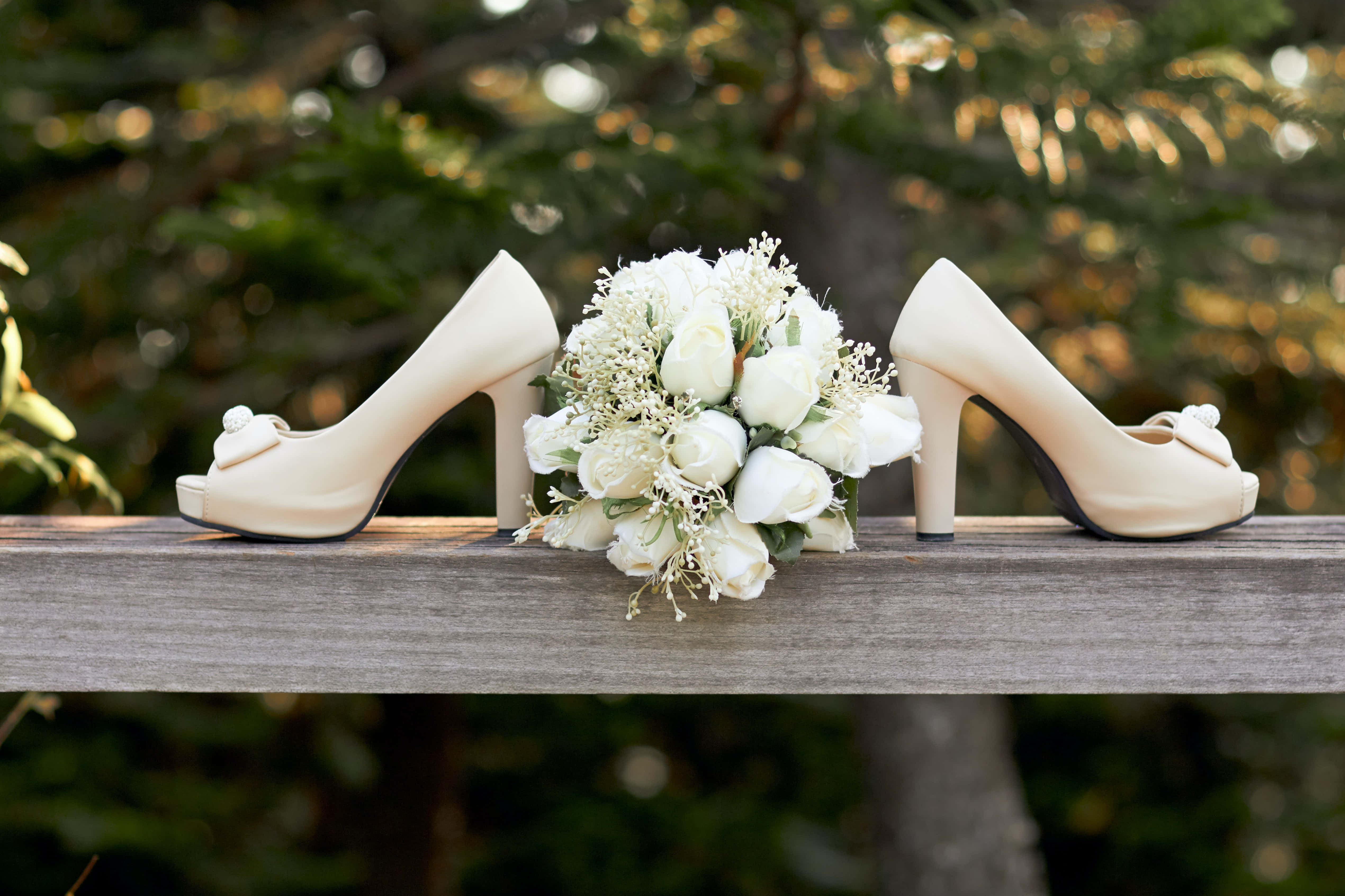 Wedding Bouquet 桌布 壁紙 — 奶油色婚禮高跟鞋和白玫瑰花束放在木欄杆上，背景是柔和的綠色散景。