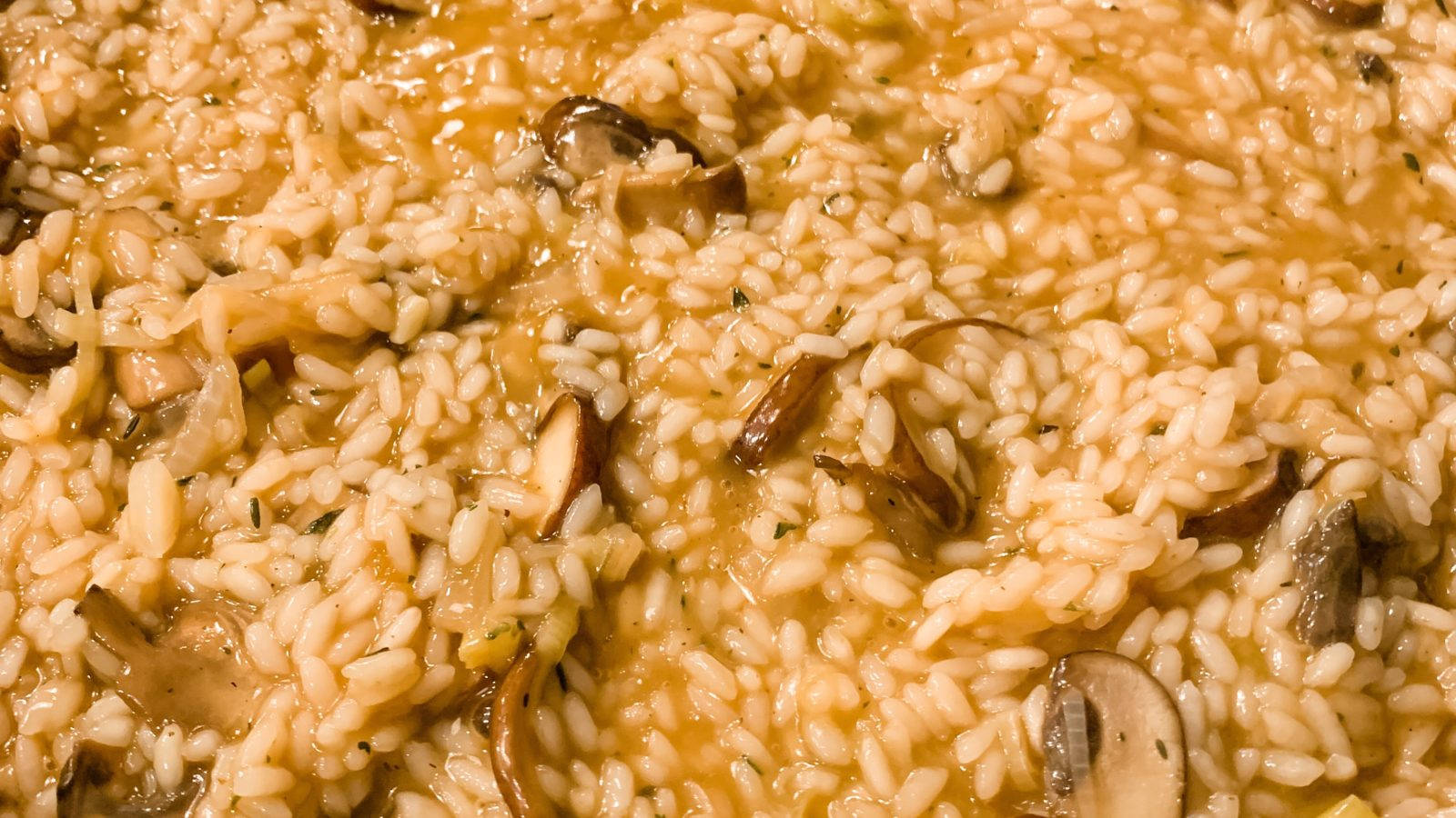mushrooms 桌布 壁紙 — 奶油蘑菇燉飯特寫，搭配金黃高湯和新鮮香草，在溫暖燈光下閃爍光芒。