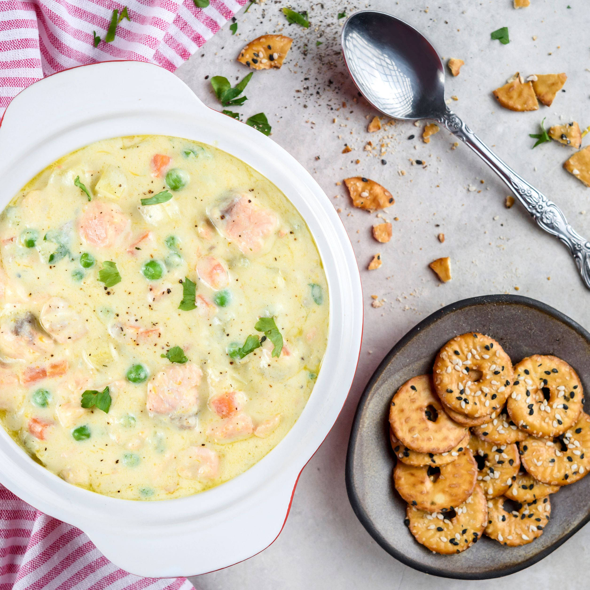 Chowder 桌布 壁紙 — 奶油鮭魚豌豆湯盛載於白色碗中，搭配芝麻薄脆餅和復古湯匙，置於淺色檯面上。