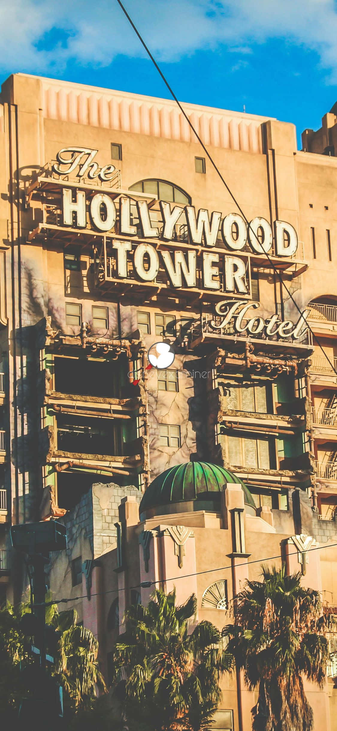 iPhone Xs California 桌布 壁紙 — 好萊塢塔酒店在明亮的藍天下聳立，薄雲飄逸，棕櫚樹在下方搖曳。