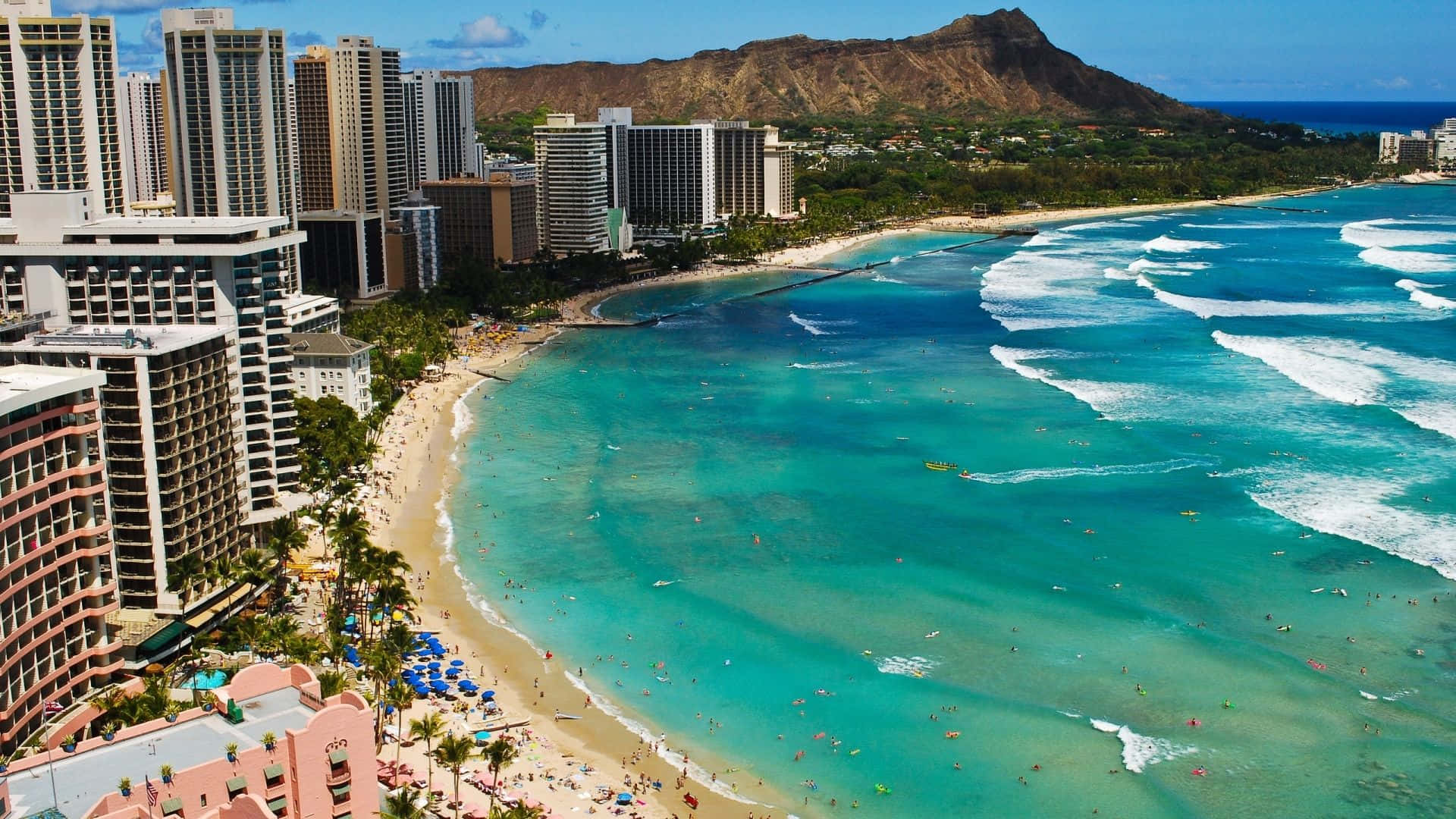 Hawaiian Beach 桌布 壁紙 — 威基基海灘的鳥瞰圖，在清澈的藍天下，碧綠的海水拍打著兩旁飯店和棕櫚樹的沙灘。