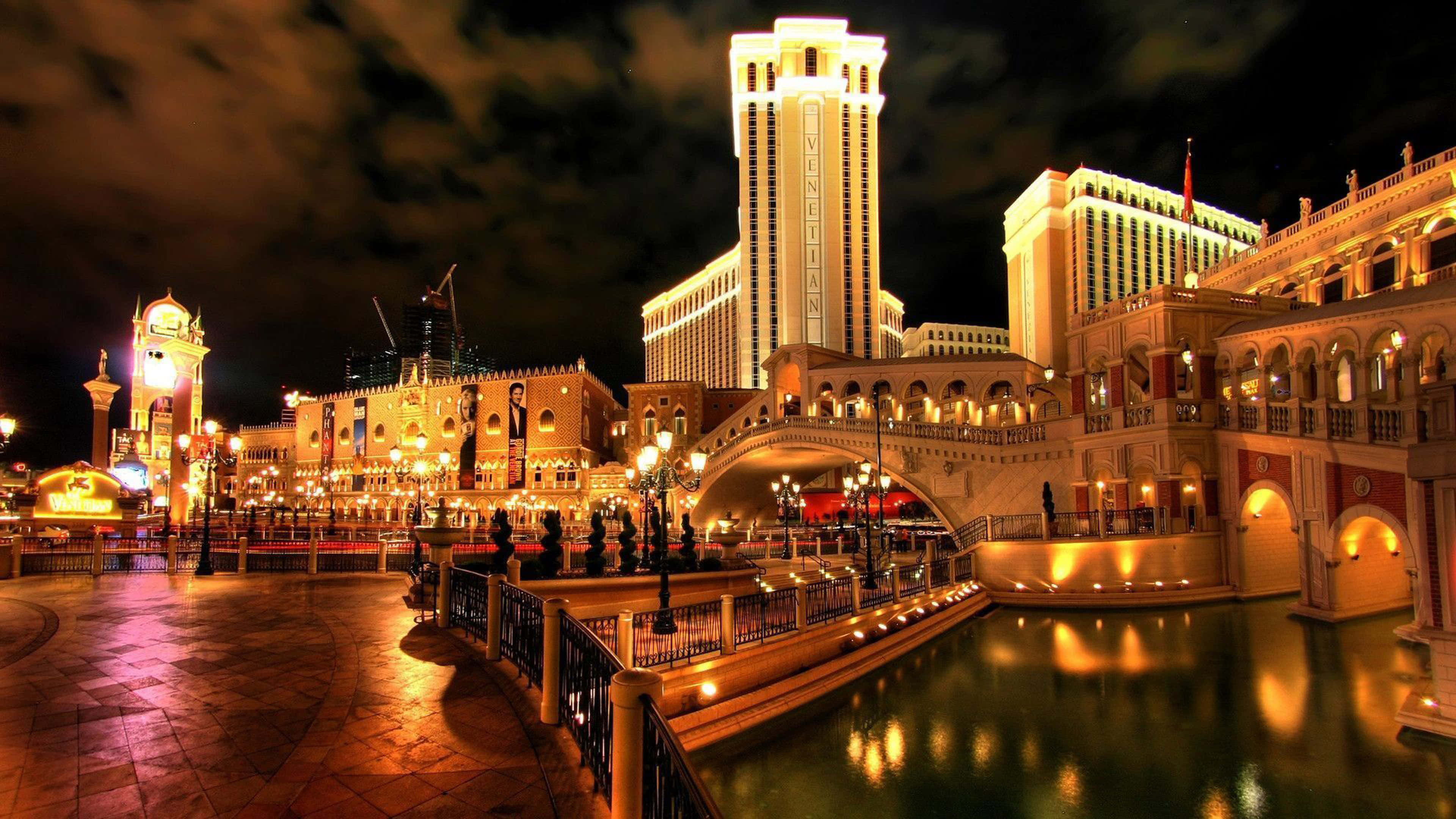 4K Las Vegas 桌布 壁紙 — 威尼斯人澳門度假村在黑暗天空下閃耀的建築和運河反射溫暖燈光的迷人夜景。