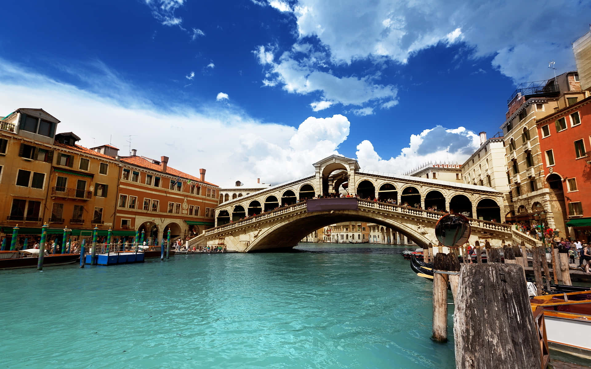 venice 桌布 壁紙 — 威尼斯標誌性的里亞爾托橋在蔚藍天空和 fluffy 白雲下，優雅地拱跨在碧綠色的運河上。