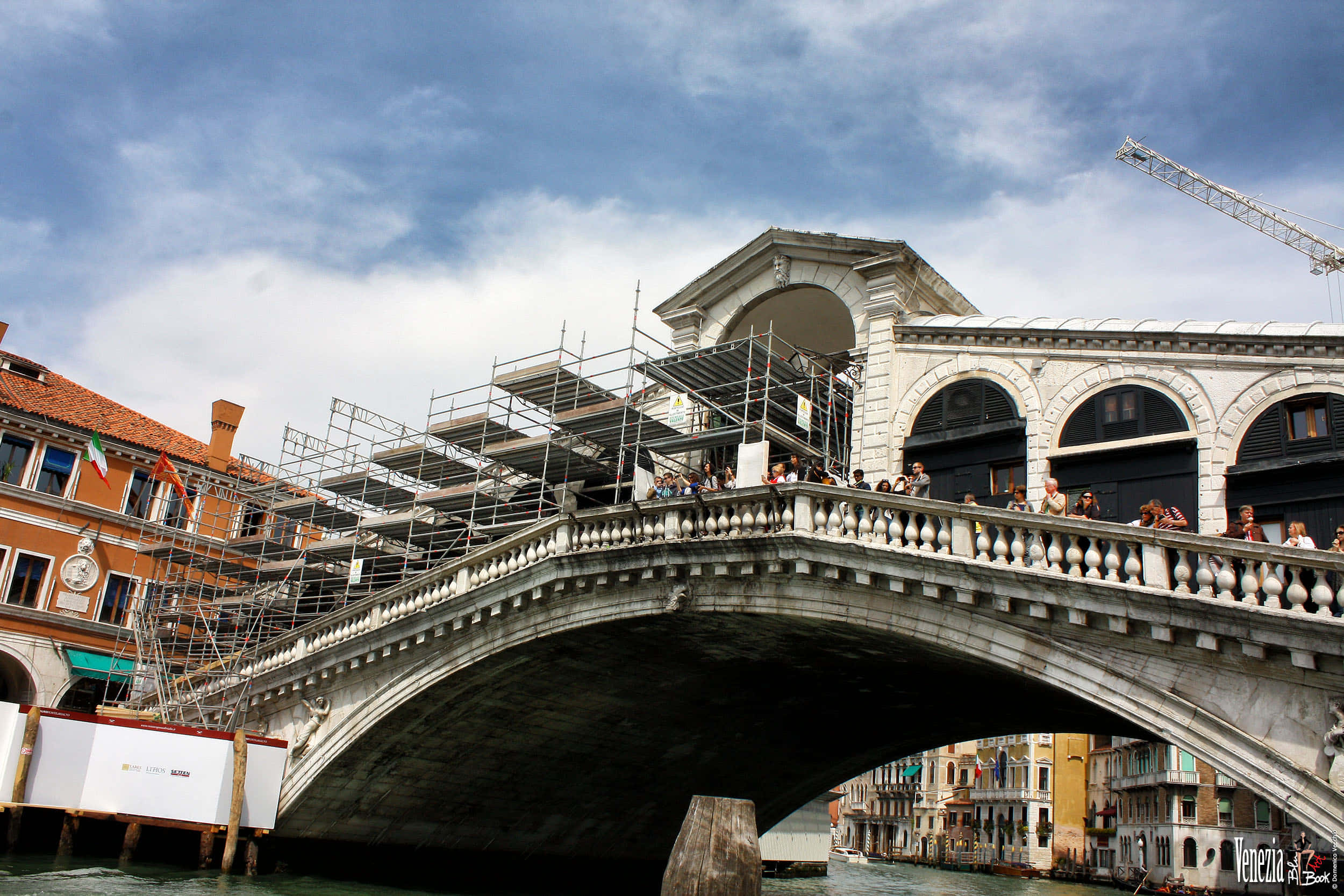 venice 桌布 壁紙 — 威尼斯標誌性的里亞爾托橋矗立在局部多雲的天空下，橋上有遊客，鷹架覆蓋了部分結構。