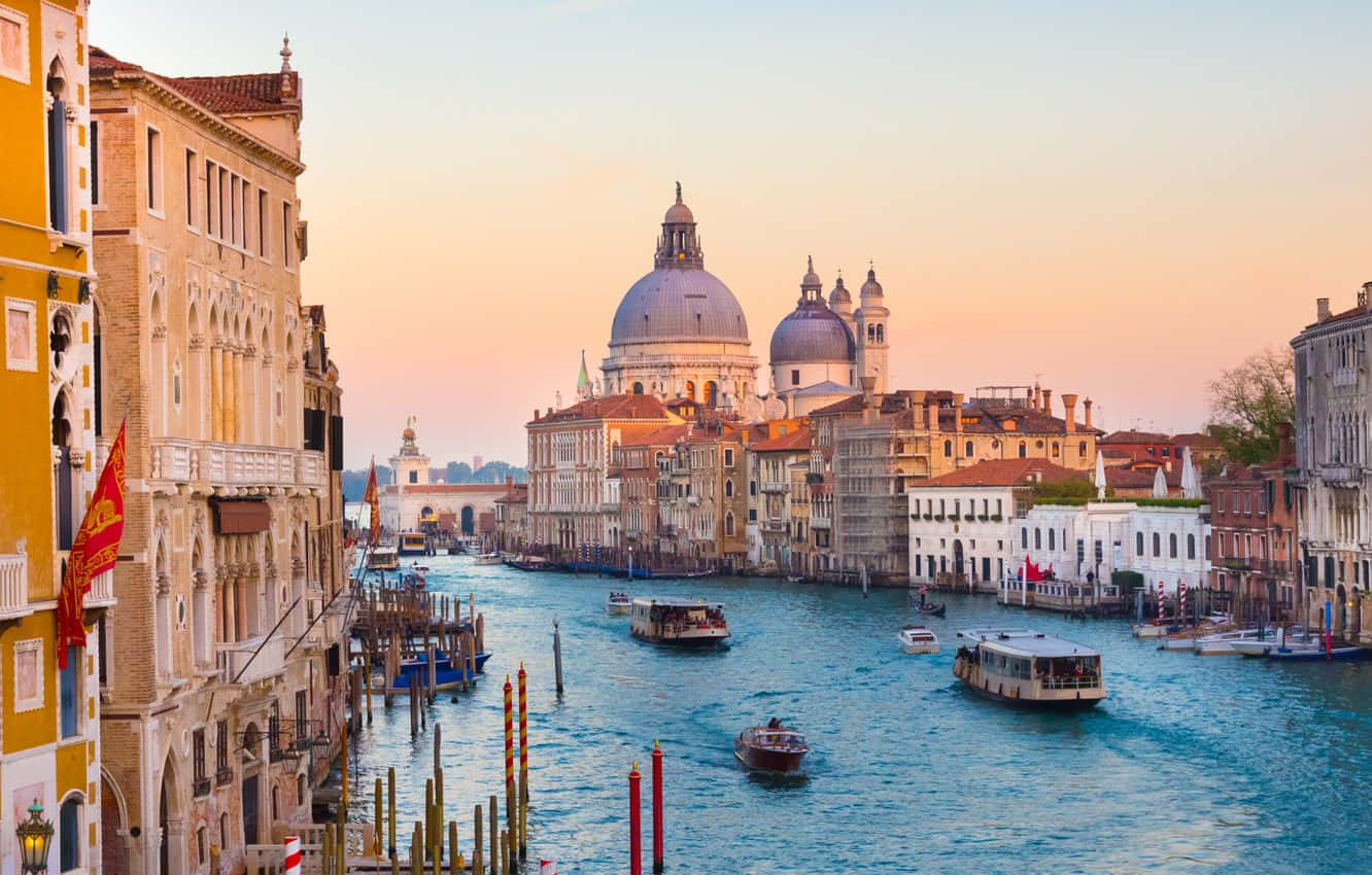 Italy Aesthetic 桌布 壁紙 — 威尼斯運河在日落時分，歷史建築、船隻和圓頂大教堂倒映在平靜的水面上。