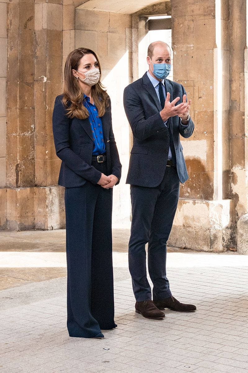 Kate Middleton 桌布 壁紙 — 威廉王子與凱特·米德爾頓站在石拱門中，戴著口罩和深色西裝，一人鼓掌，另一人靜止不動。
