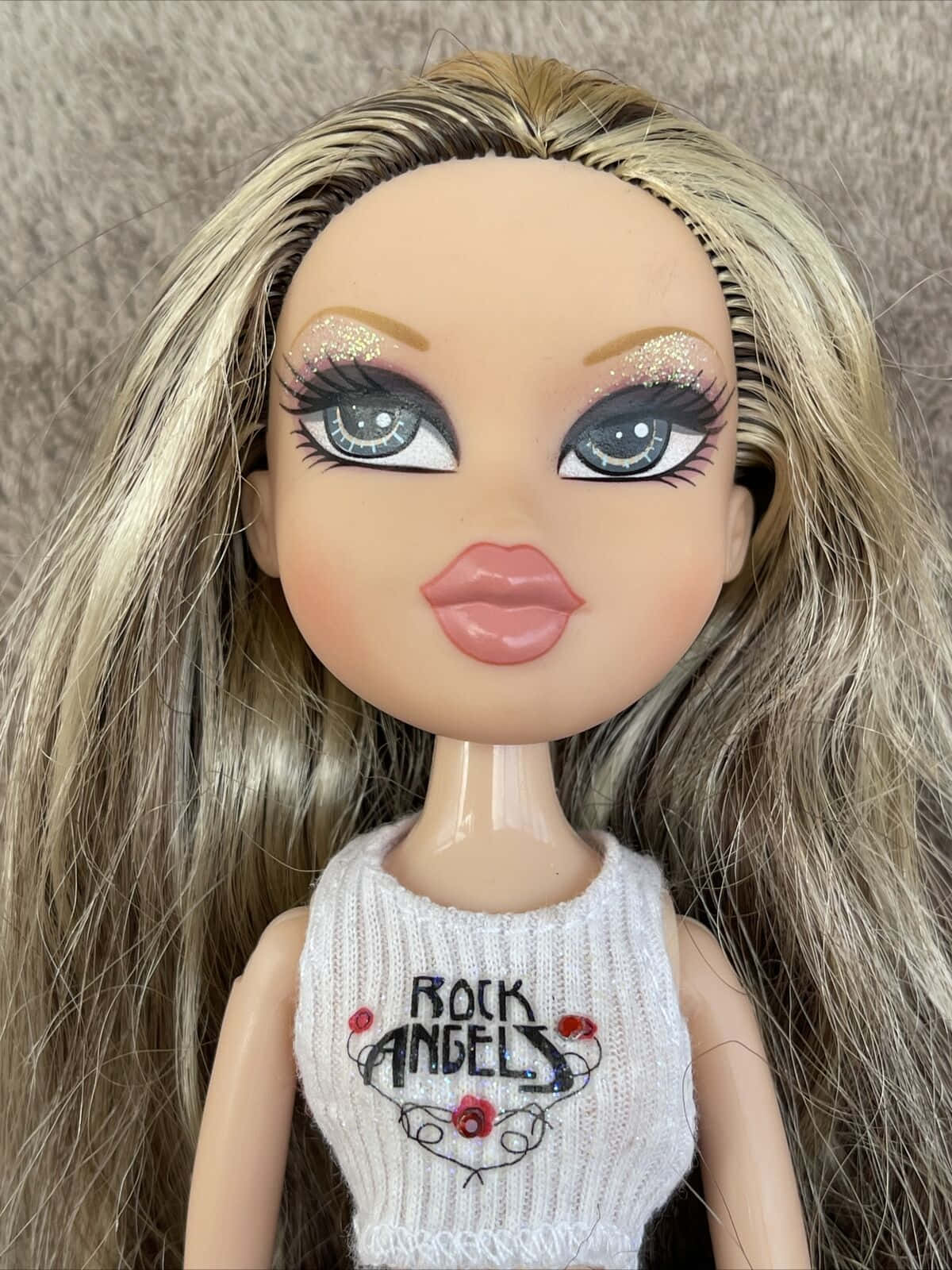 bratz 美學 桌布 壁紙 — 娃娃的特寫，有長長的金色頭髮、閃閃發光的眼睛，以及一件寫著 rock angels 的白色針織上衣。
