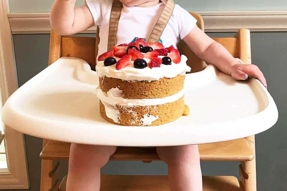 Birthday Cake 桌布 壁紙 — 嬰兒在高腳椅上伸手去拿一個兩層蛋糕，上面有草莓和藍莓。