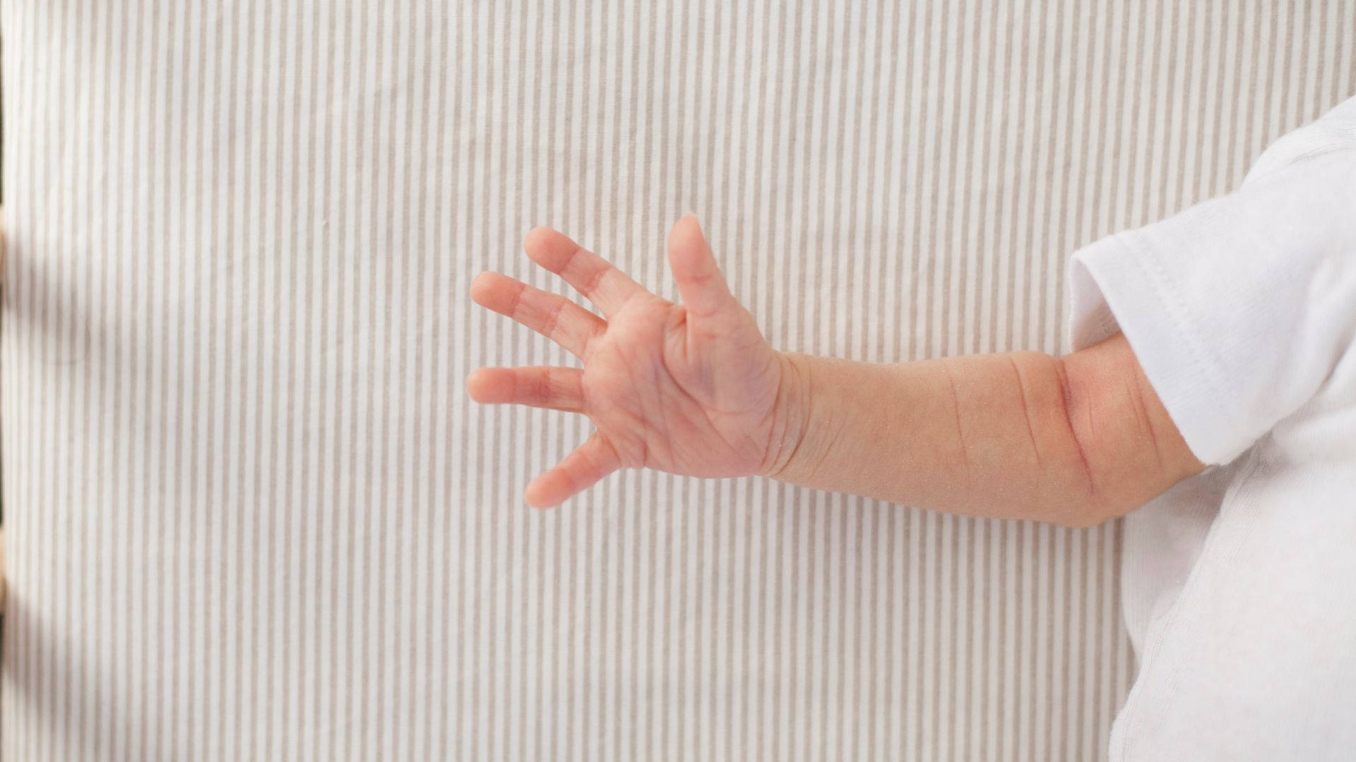 嬰兒的手伸向條紋布料背景。 — 烏賈因 馬哈卡爾 壁紙
