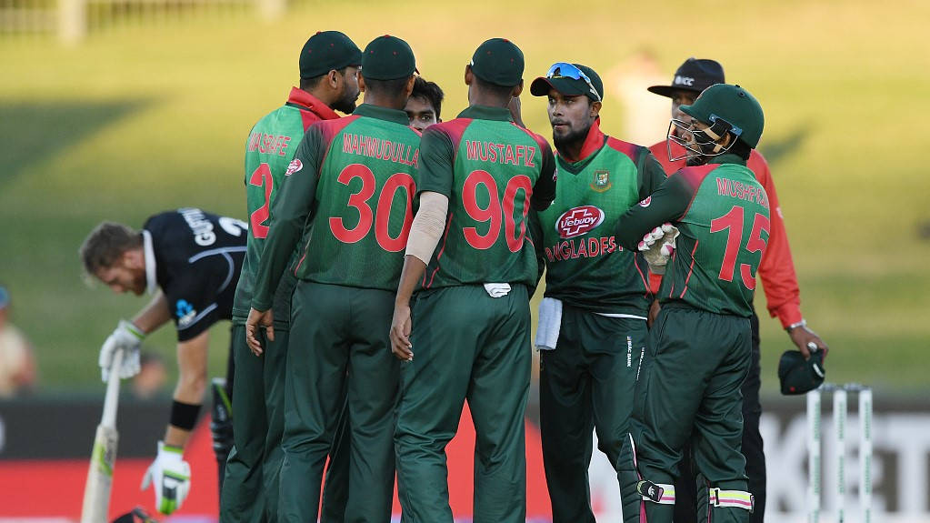 Bangladesh Cricket 桌布 壁紙 — 孟加拉國板球隊在陽光明媚的草地上穿著綠色制服，上面有紅色號碼，在比賽中聚集。