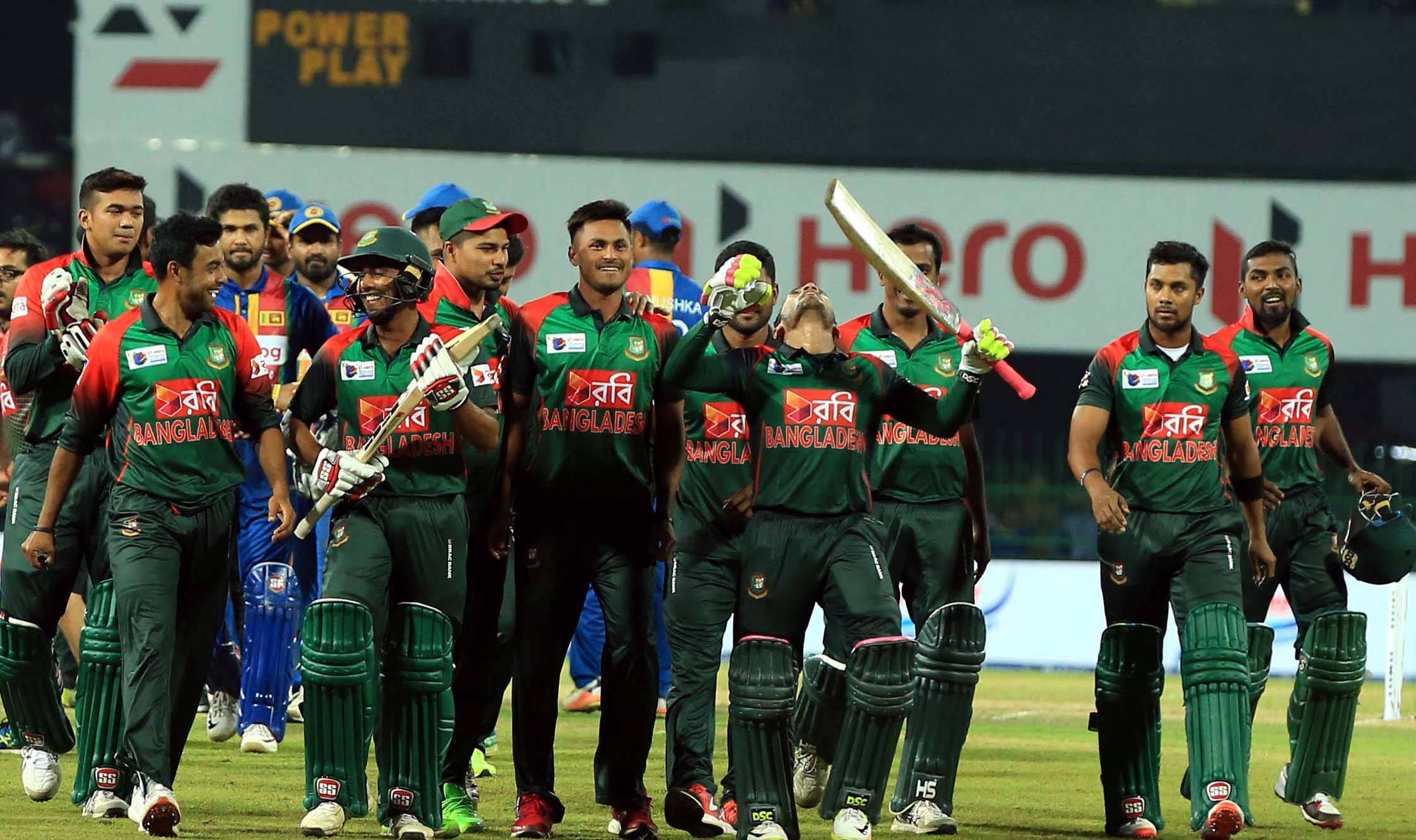 Bangladesh Cricket 桌布 壁紙 — 孟加拉國板球隊在體育場燈光下的綠色場地上慶祝勝利，手持球棒和頭盔。