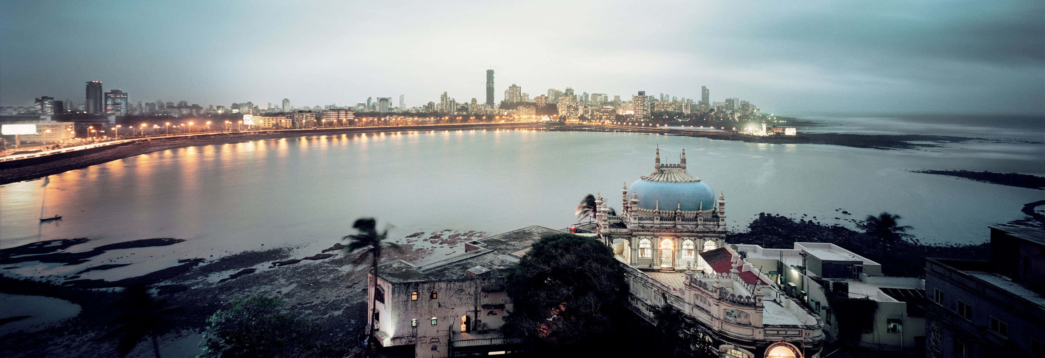 Mumbai 桌布 壁紙 — 孟買海岸線的黃昏全景，閃爍的城市天際線和前景的圓頂寺廟。