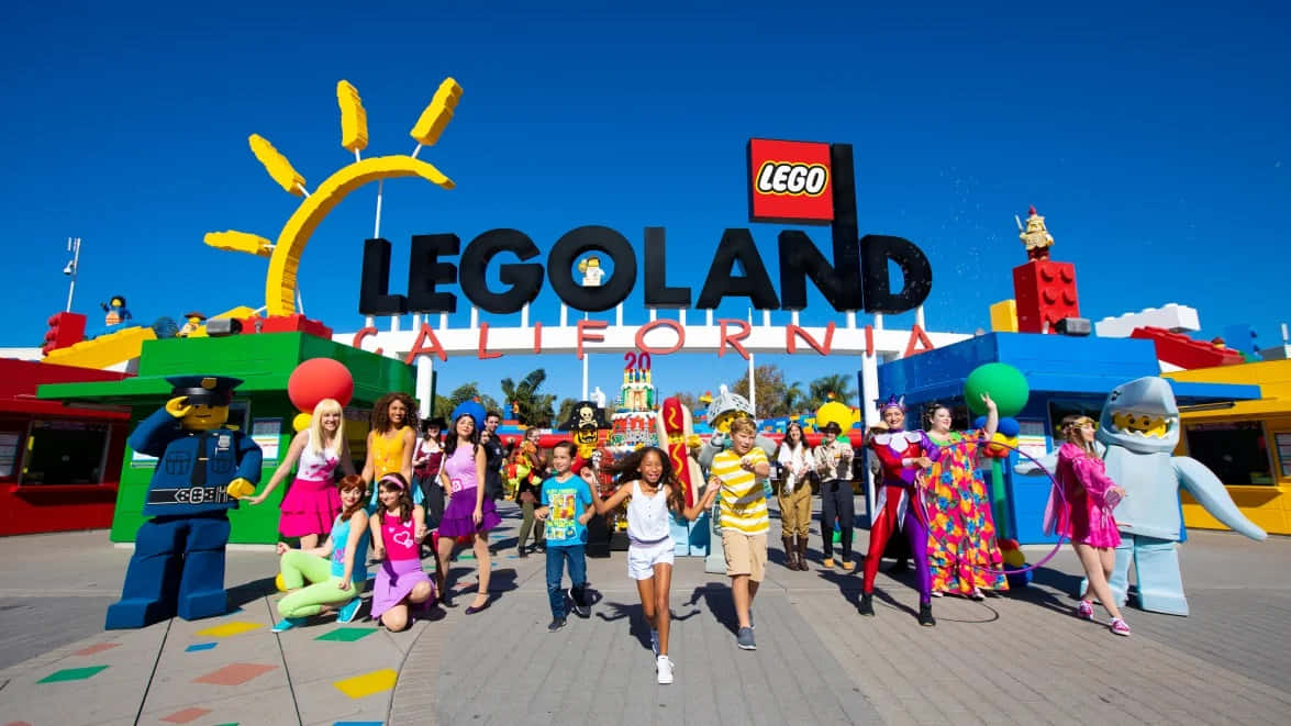 Legoland 桌布 壁紙 — 孩子們和LEGO角色在LEGOLAND California色彩繽紛的入口處，在明亮的藍天下愉快地擺姿勢。