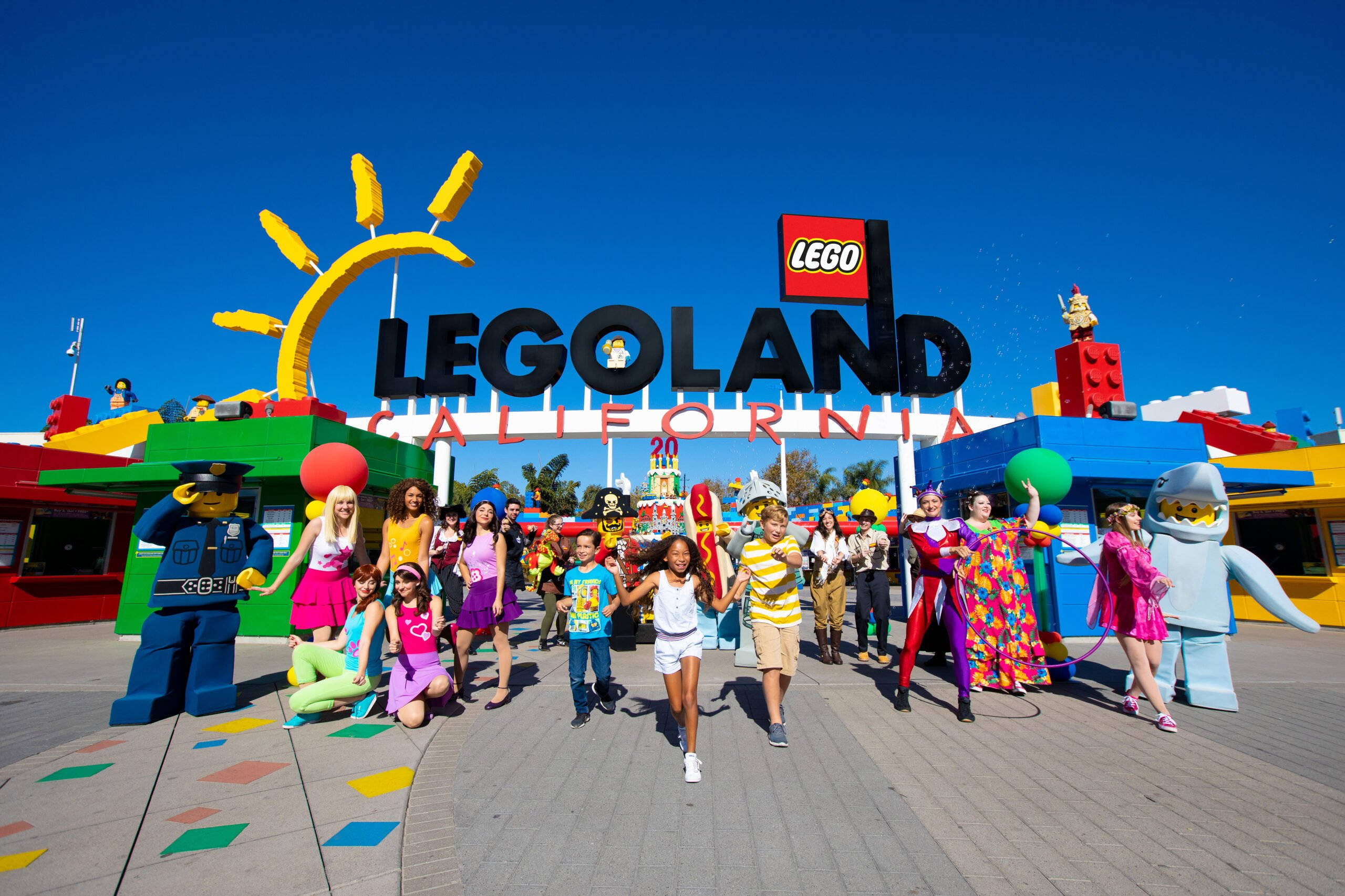 小孩動圖 桌布 壁紙 — 孩子們和LEGO角色在明亮的藍天下，於LEGOLAND California色彩繽紛的入口處愉快地擺姿勢。